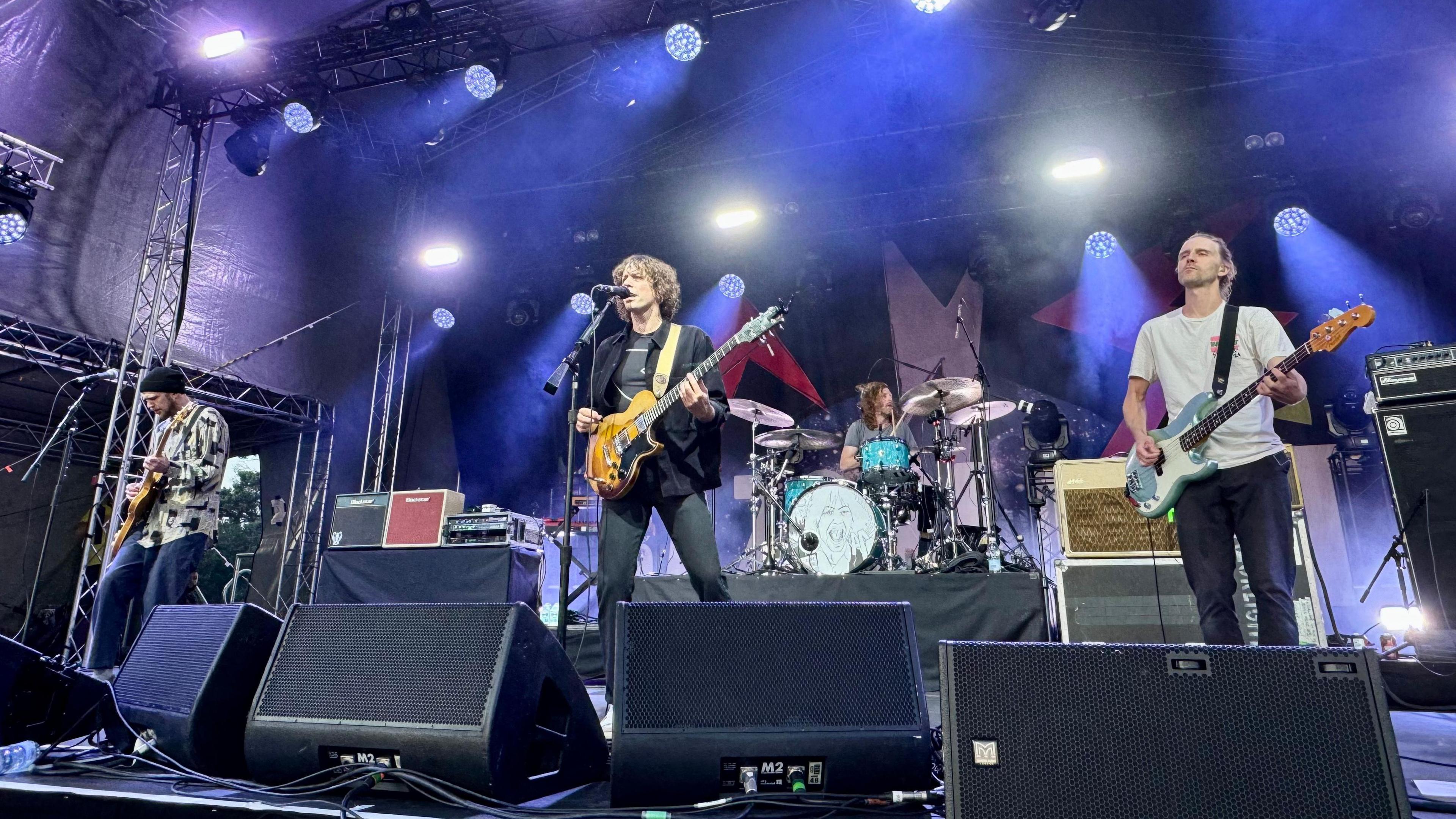 Razorlight performing on stage with purple lighting and three guitarists at the front and a drummer with a turquoise kit on a riser behind them