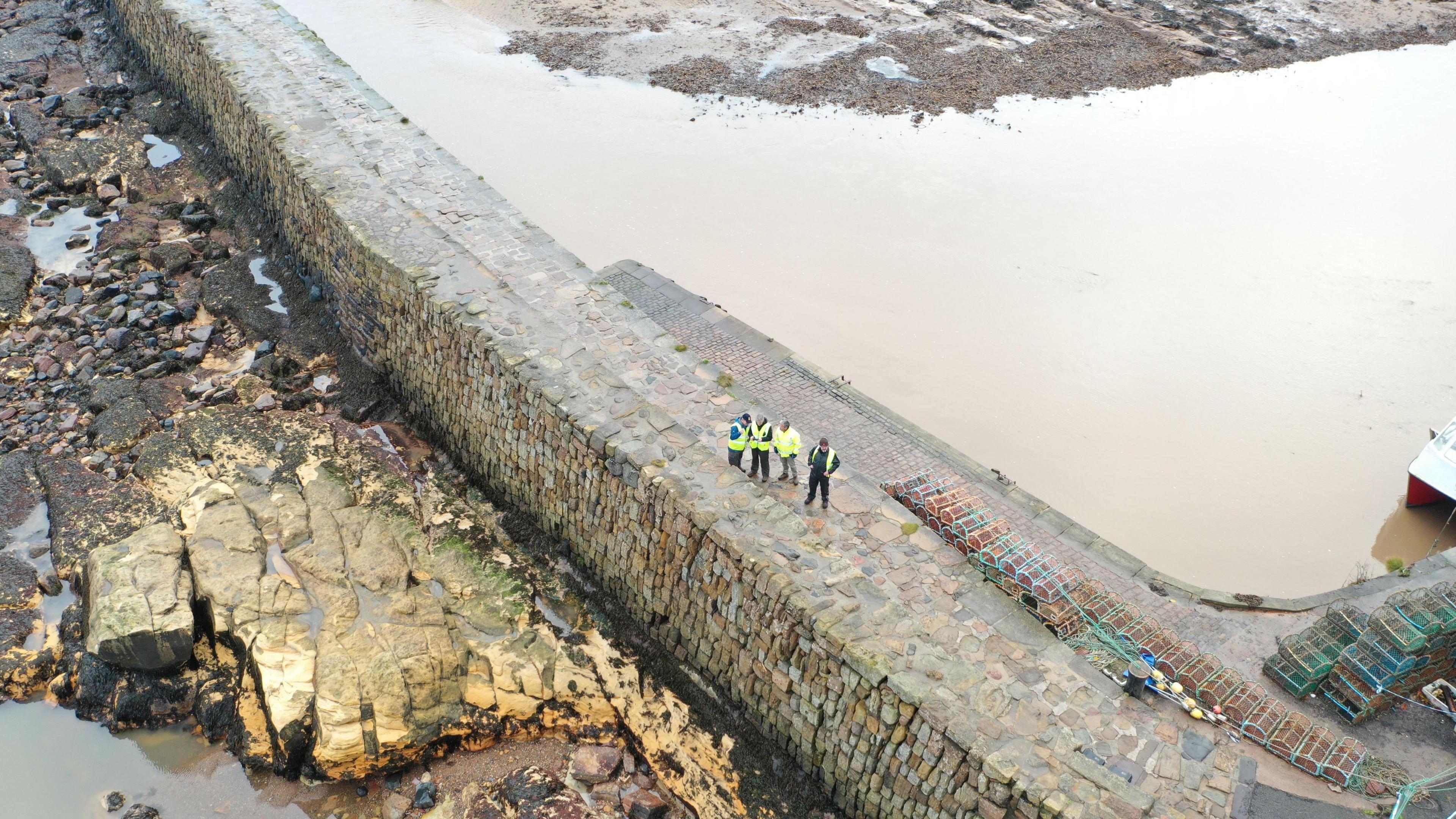 A drone shot of the pier with people in hi-vis tops standing on it