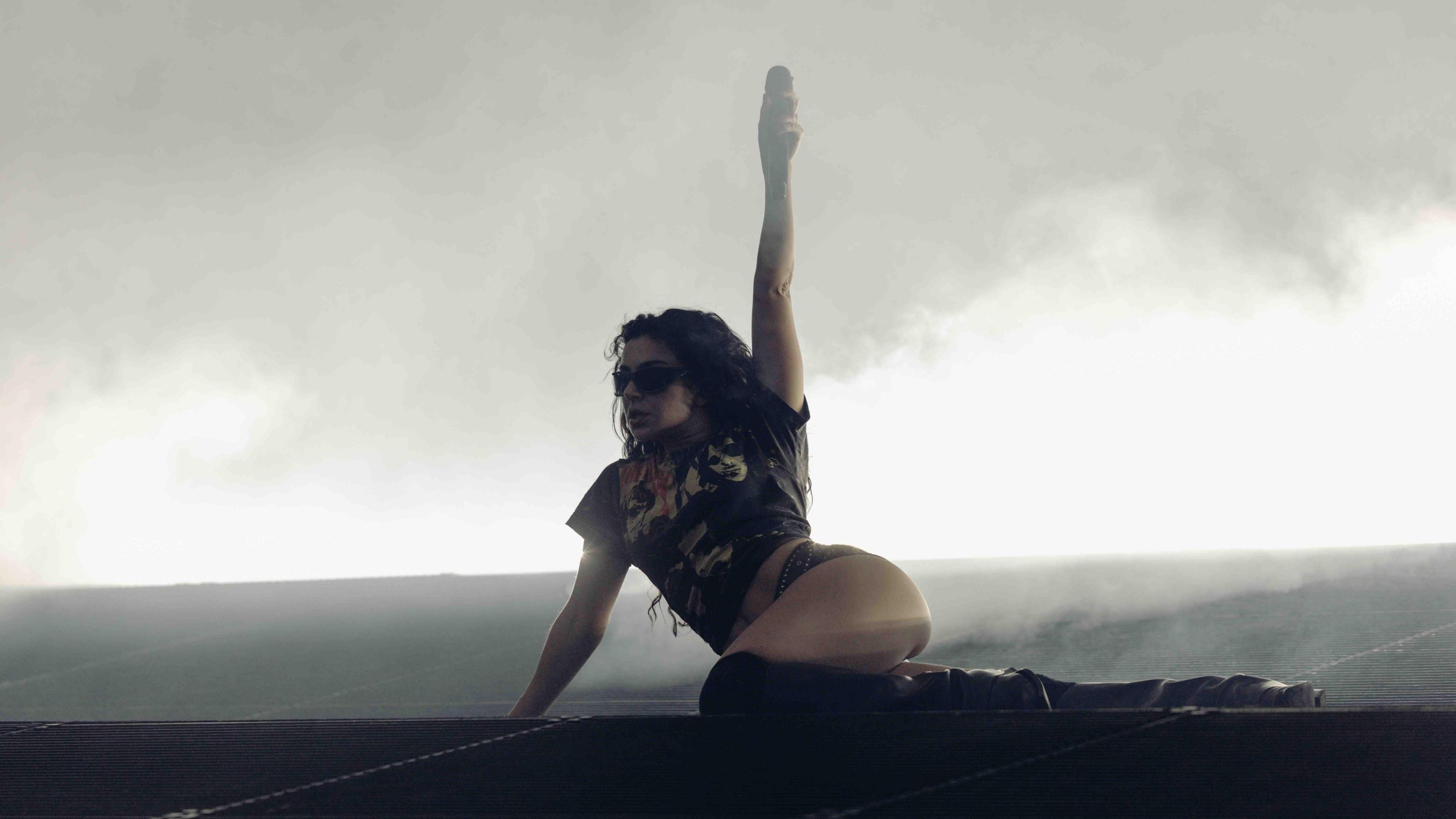 Charli XCX on stage at Belsonic. She wears knee high boots, shorts and a black t shirt. There is smoke behind her.