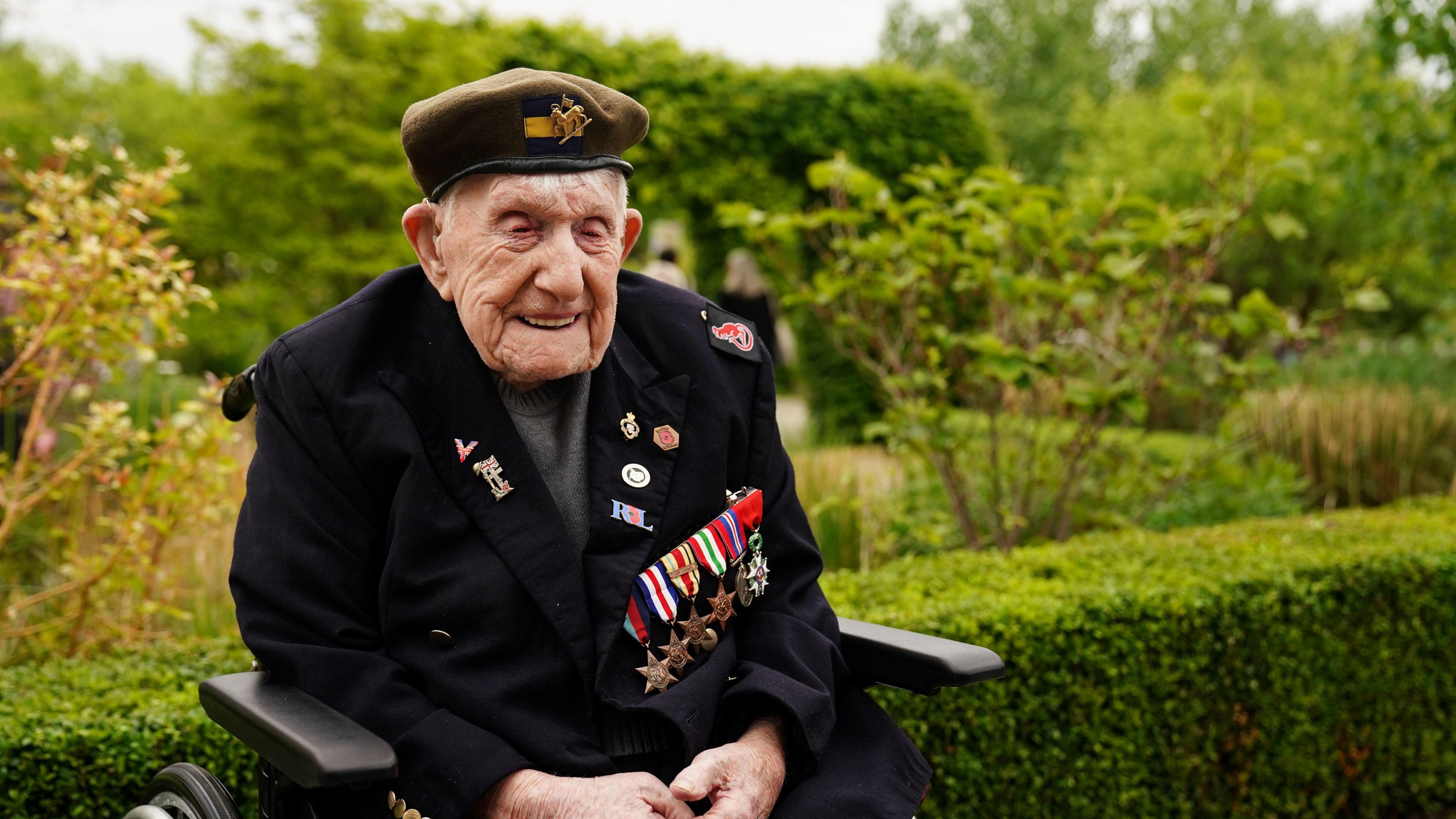 Donald Rose, sitting in a wheelchair in front of a garden, wears his military medals and beret.