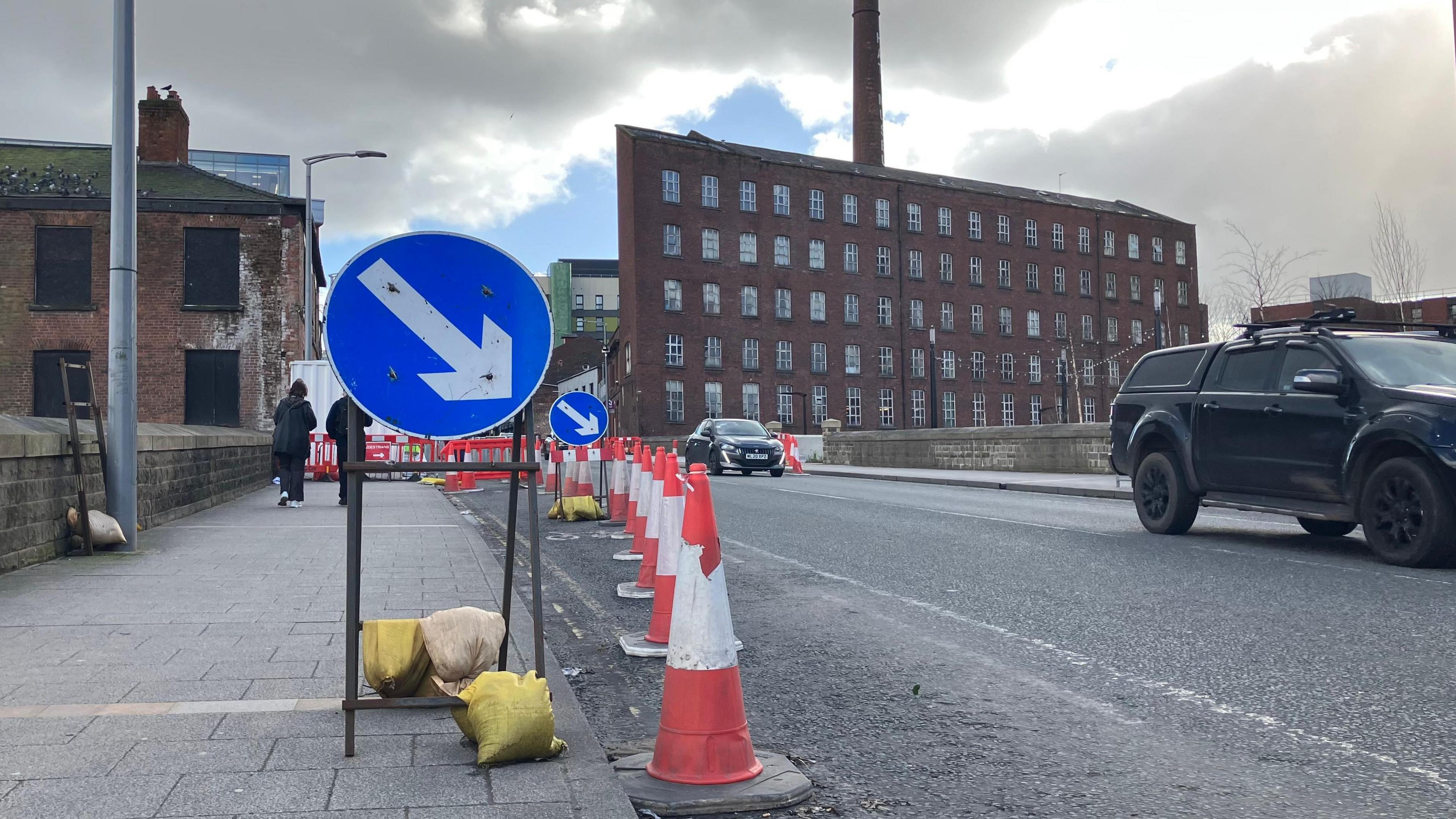 Blue-and-white road signs and red-and-white traffic cones denote an area of roadworks.