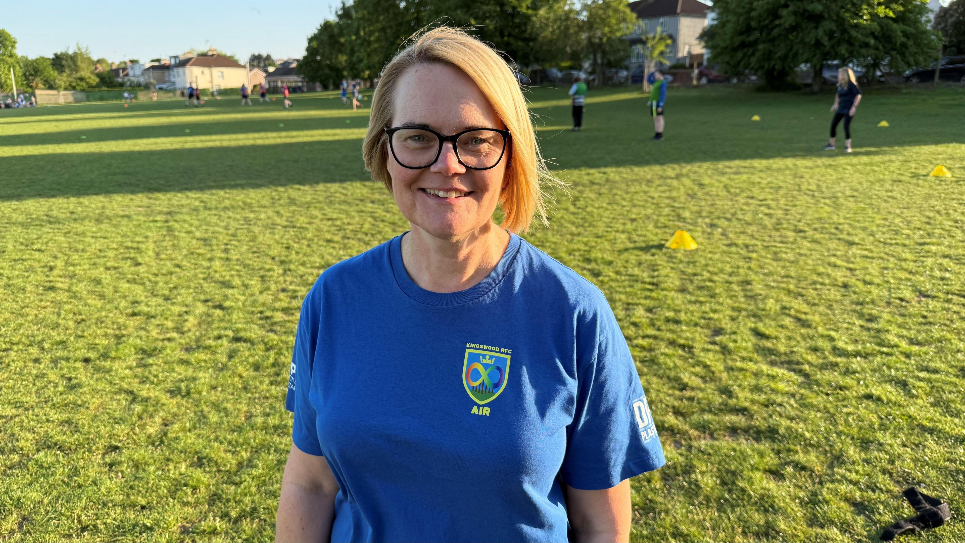 Louise Sims in front of the AIR team training pitch in a blue Kingswood AIR t shirt.