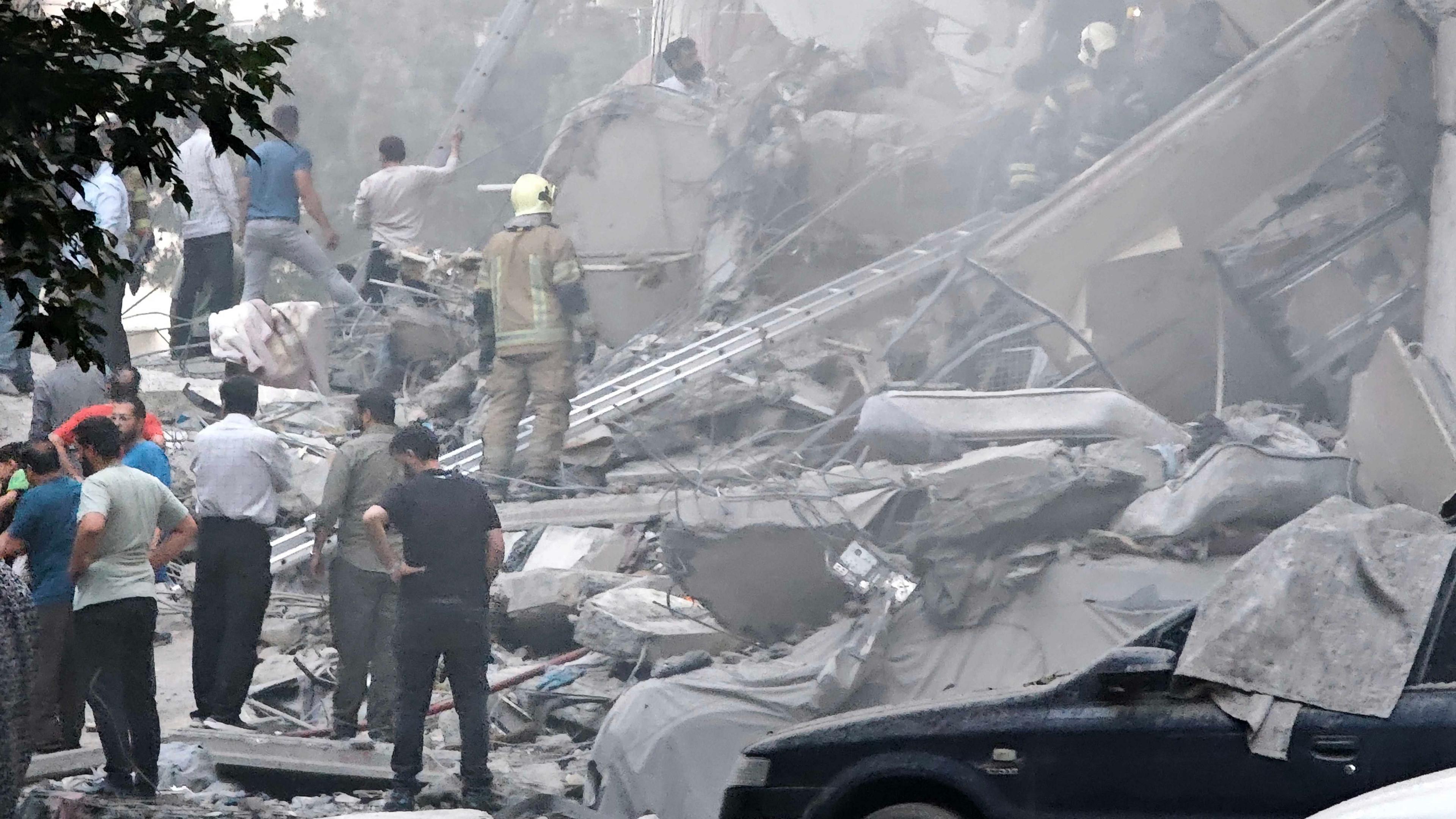 People look over damage to buildings in Nobonyad Square following Israeli air strikes