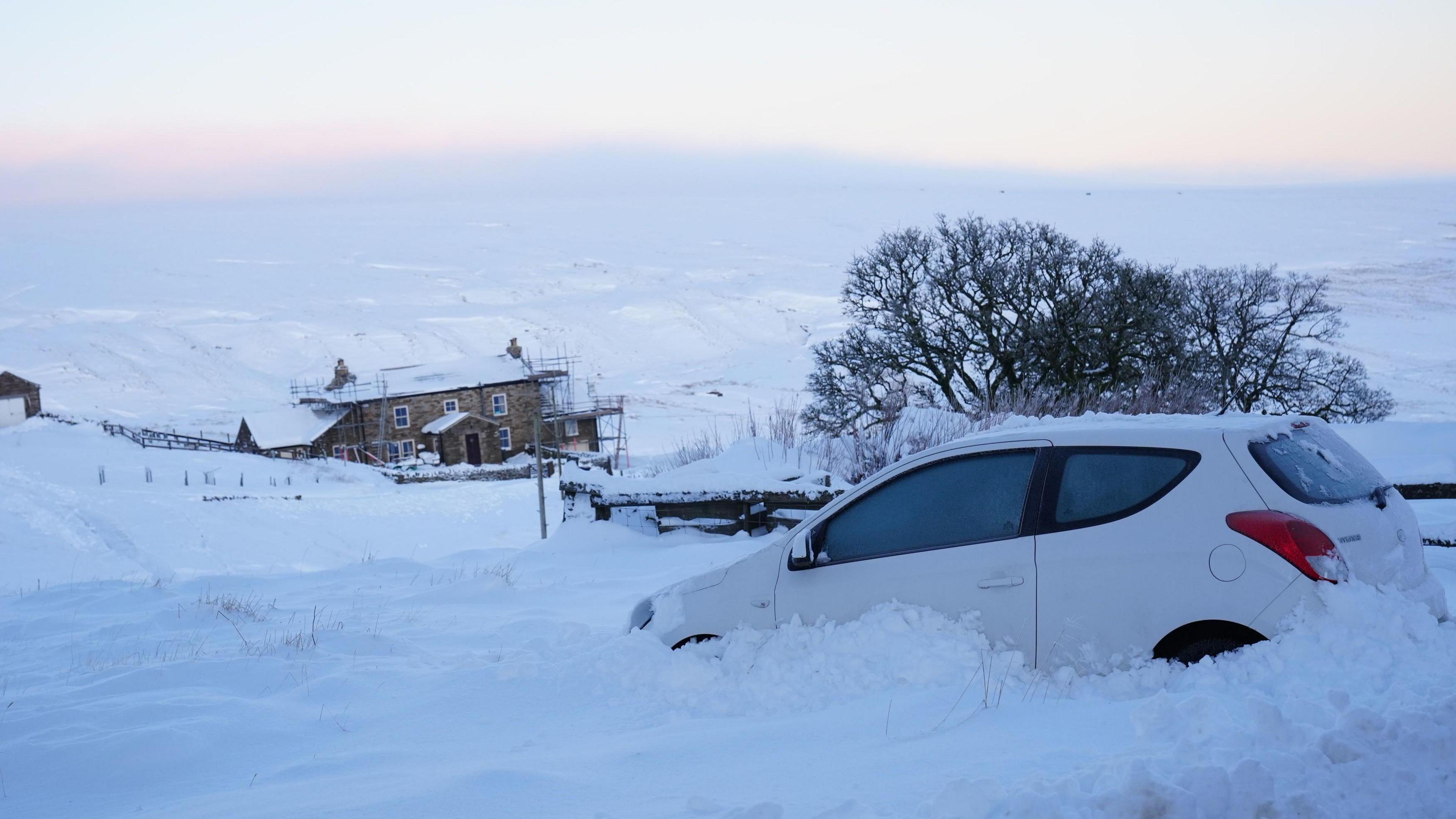 A car is stuck in deep snow in rural Northumberland, with a house visible in the distance