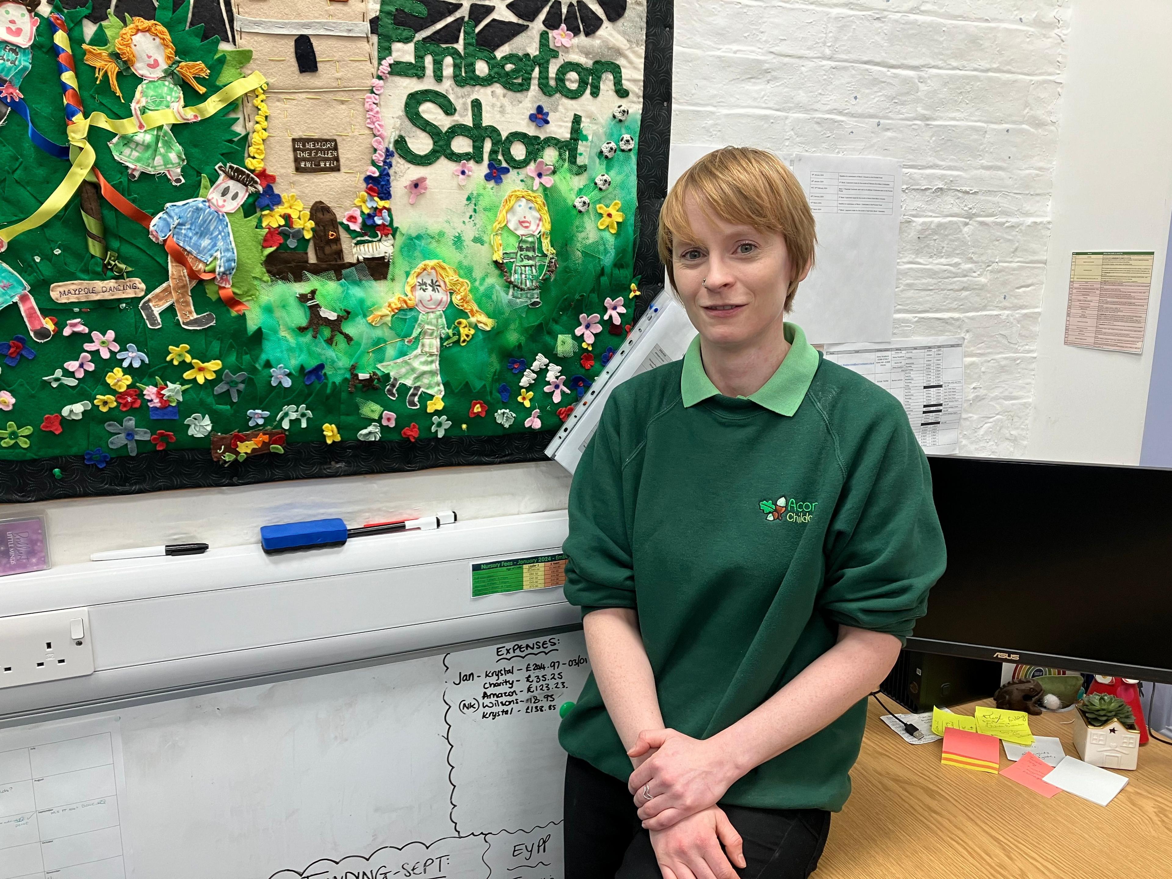 A picture of a woman with short blonde hair who is wearing a green jumper