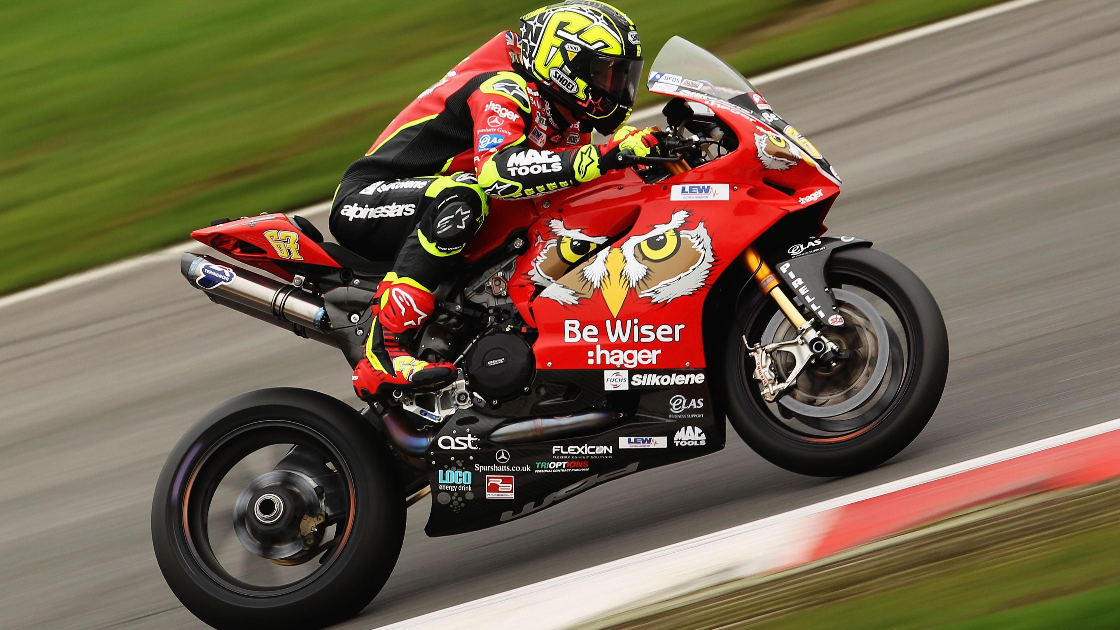 Shane Byrne on a motorcycle on a track. The motorbike is red, with the crest of a bird's face on the side - either an owl or an eagle.