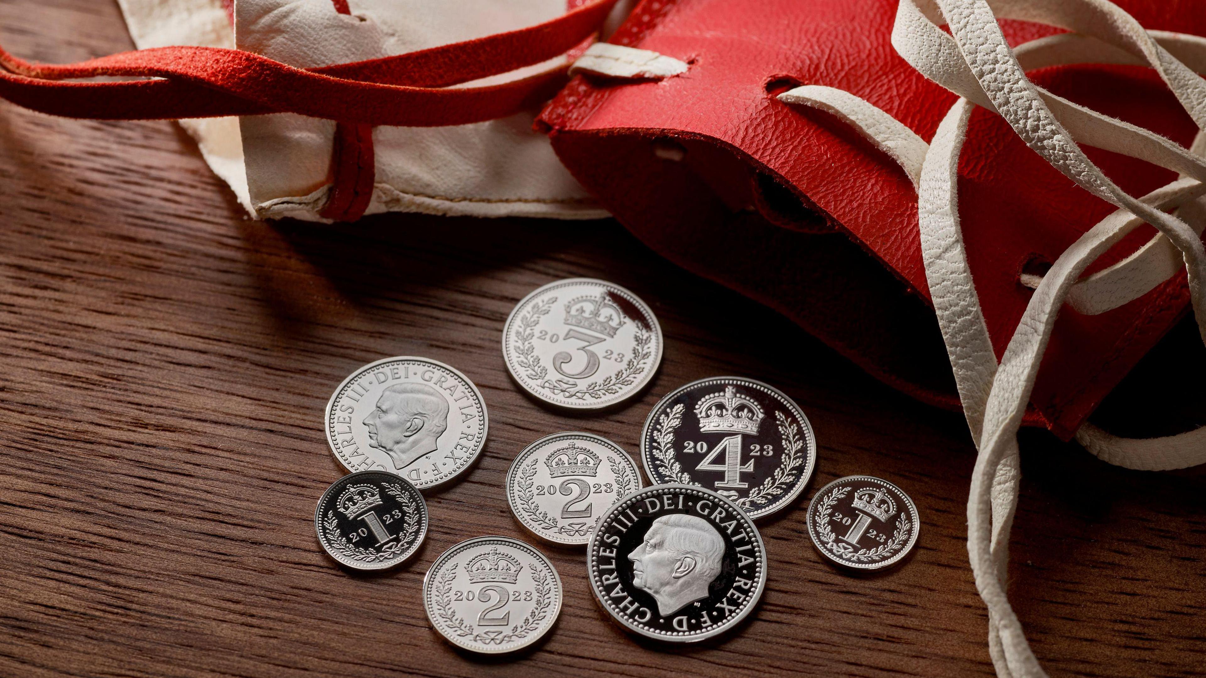 Various coins with the head of King Charles III alongside the red Maundy purse.