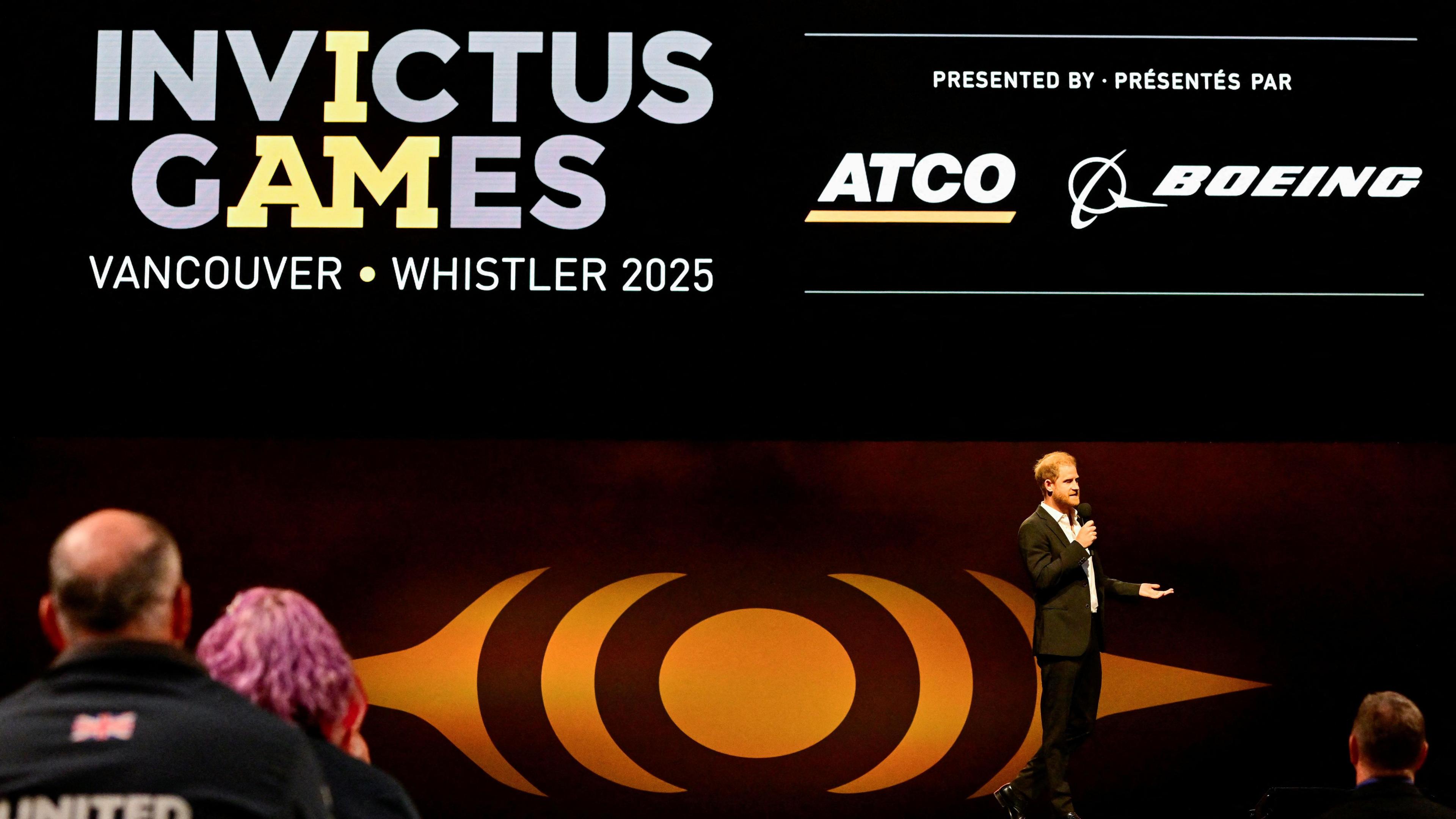 Prince Harry talking to a crowd wearing a dark suit in front of signage for the Invictus Games, which has just taken place in Vancouver and Whistler, Canada