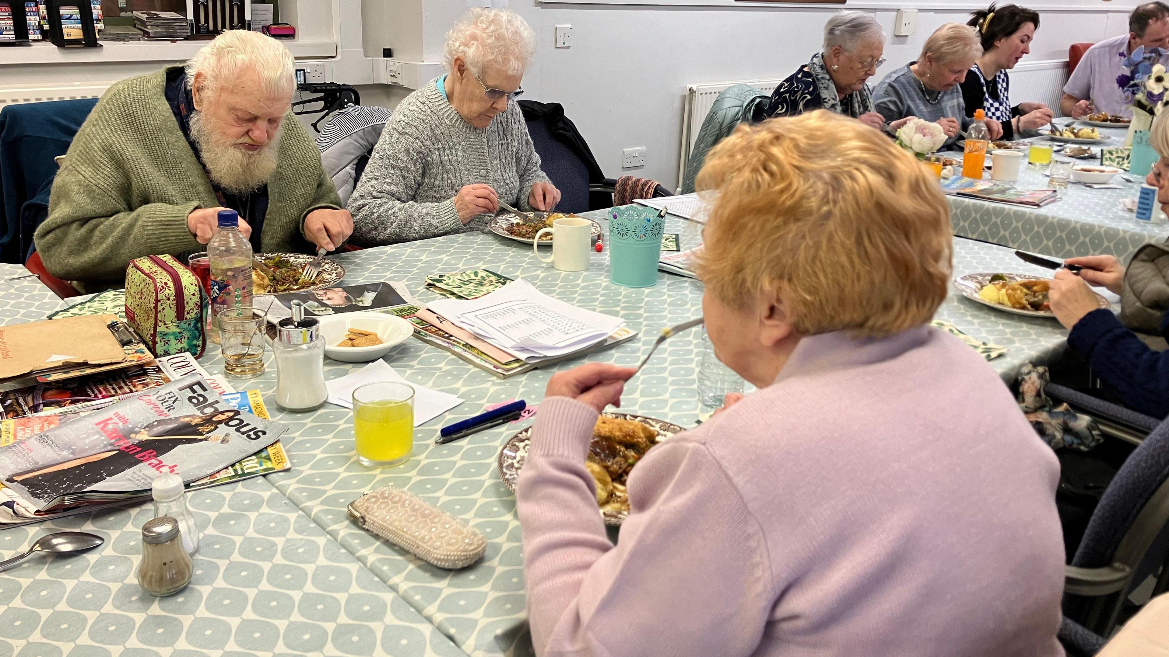 Older people sitting around two tables tucking into lunch.