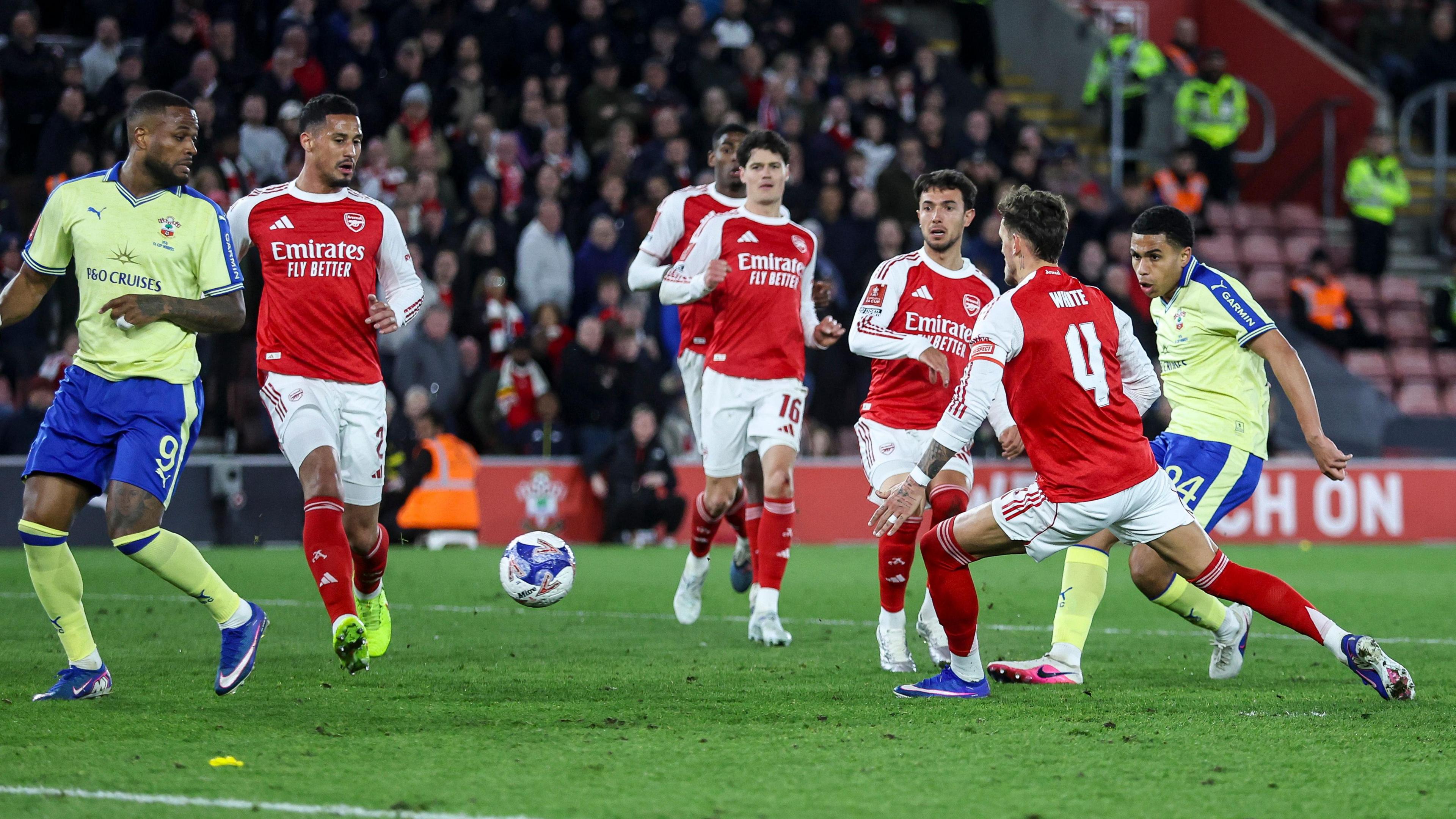 Shea Charles scores against Arsenal, firing a shot as Gunners players in red and white look on