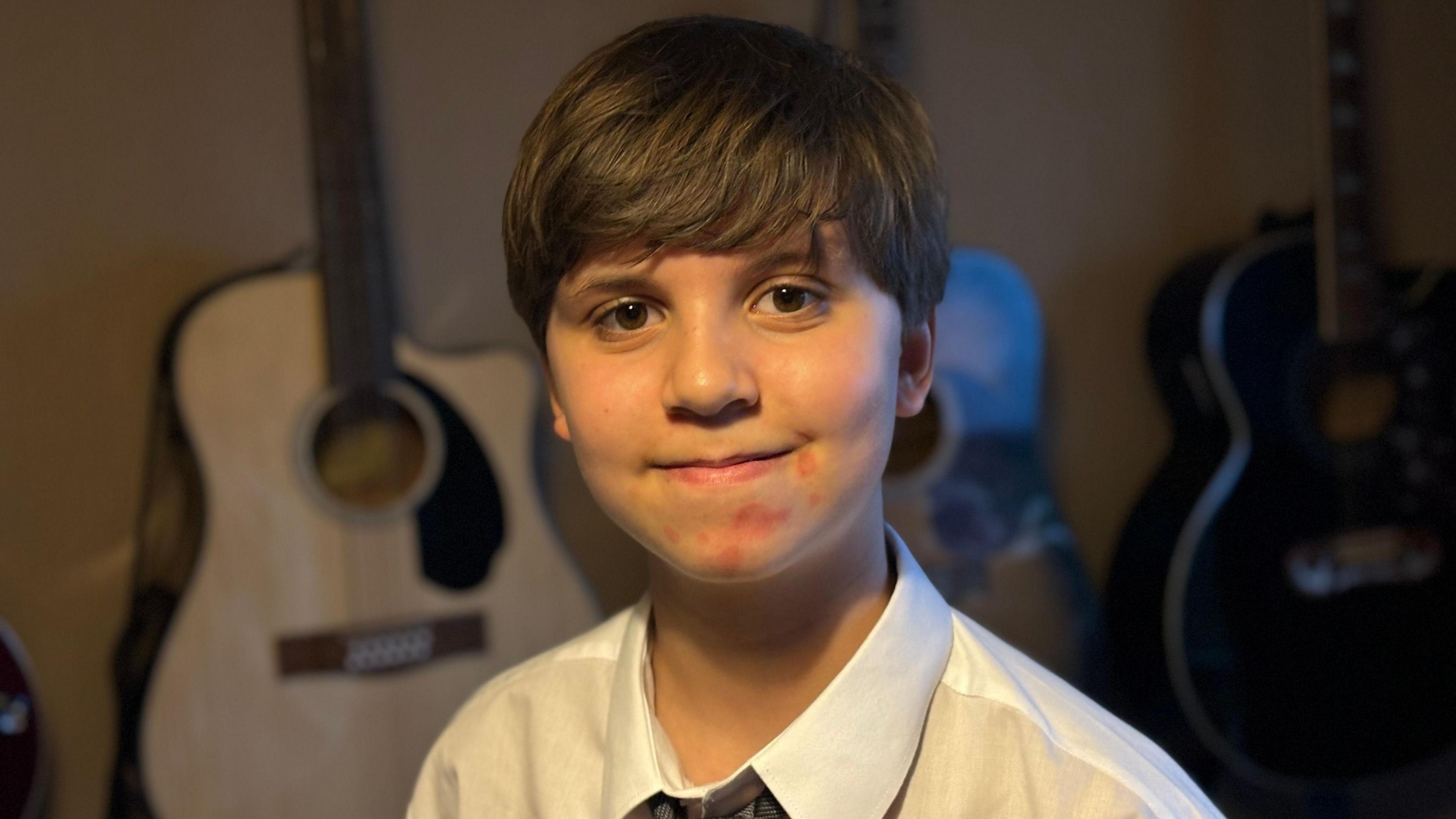 Llun o Celyn yn gwenu ar y camera. Mae sawl gitar yn y cefndir.