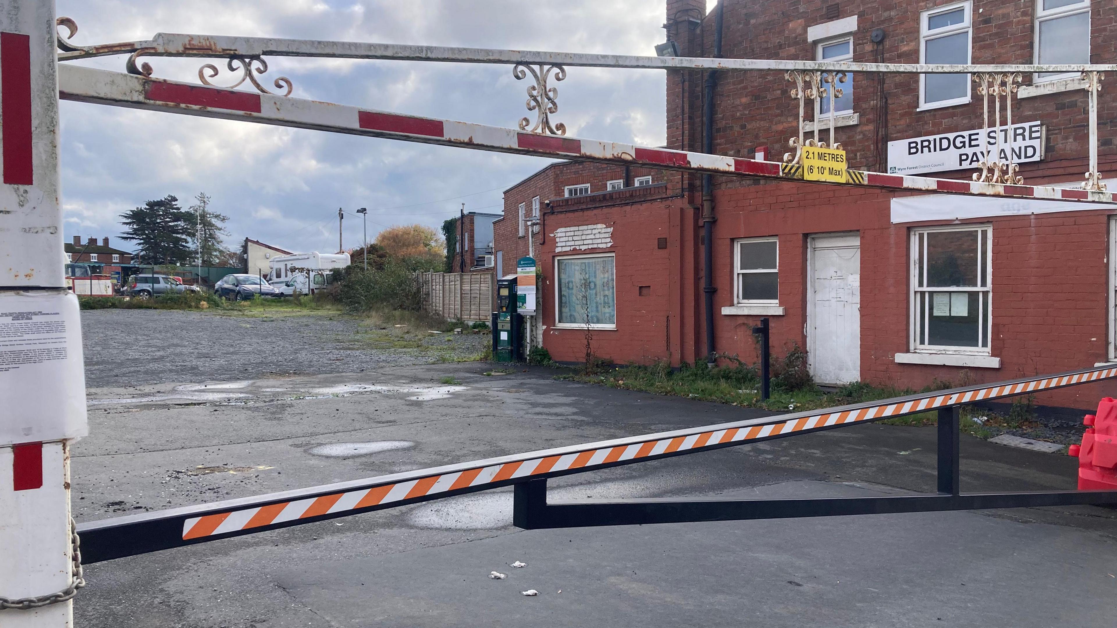 A metal barrier preventing vehicles from parking on a piece of land covered in tarmac.
