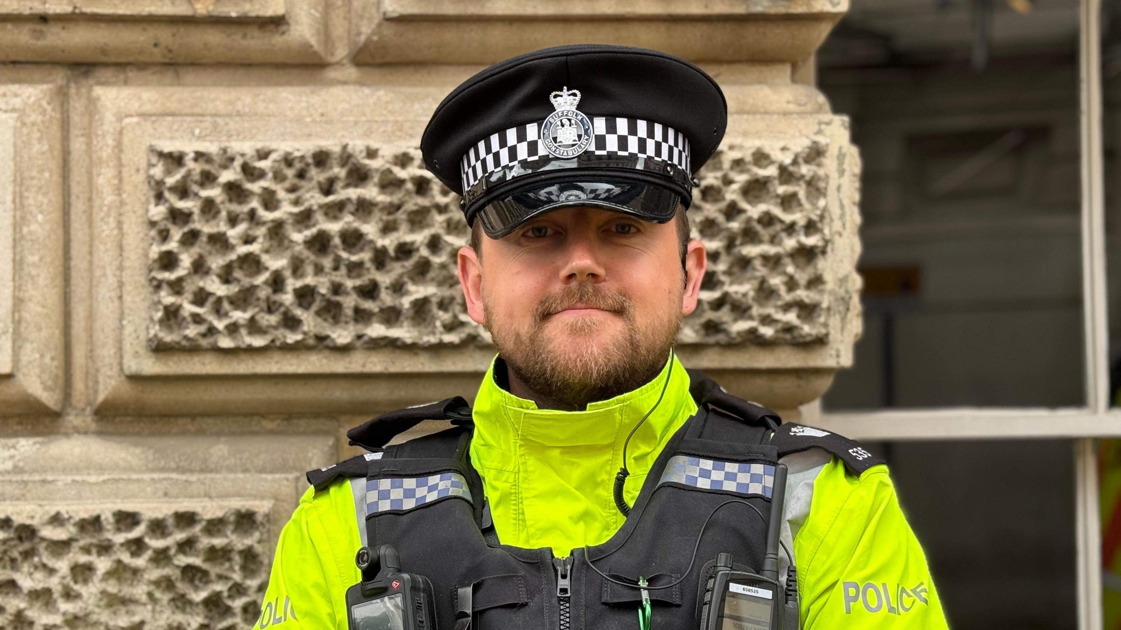 A close-up head and shoulders image of PC Lewis Finch. He has a dark beard and is smiling. He is wearing a police uniform and looking straight into the camera.