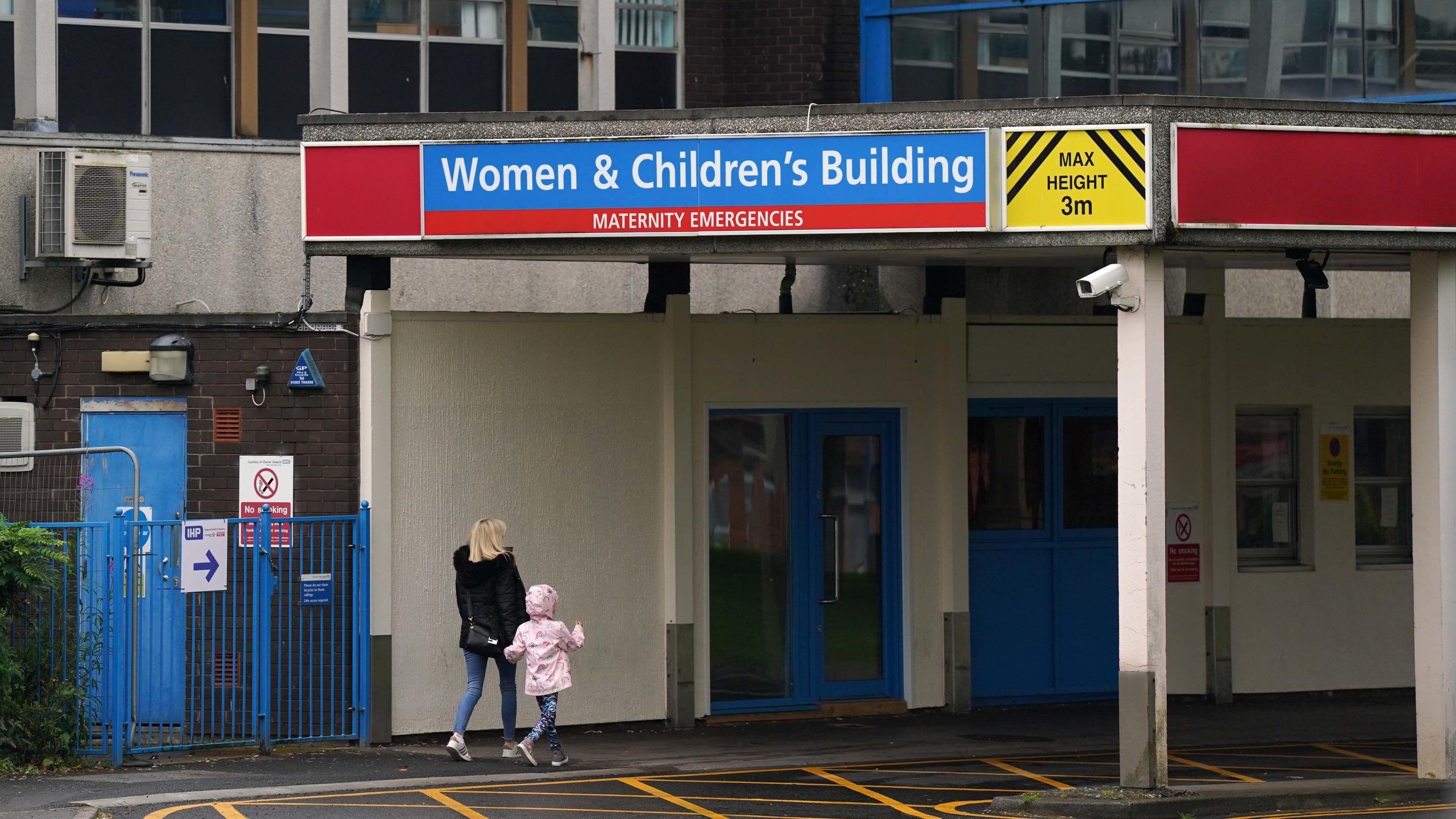 A woman with blonde hair walks into the Women & Children's building at the Countess of Chester holding hands with a little girl in a pink coat