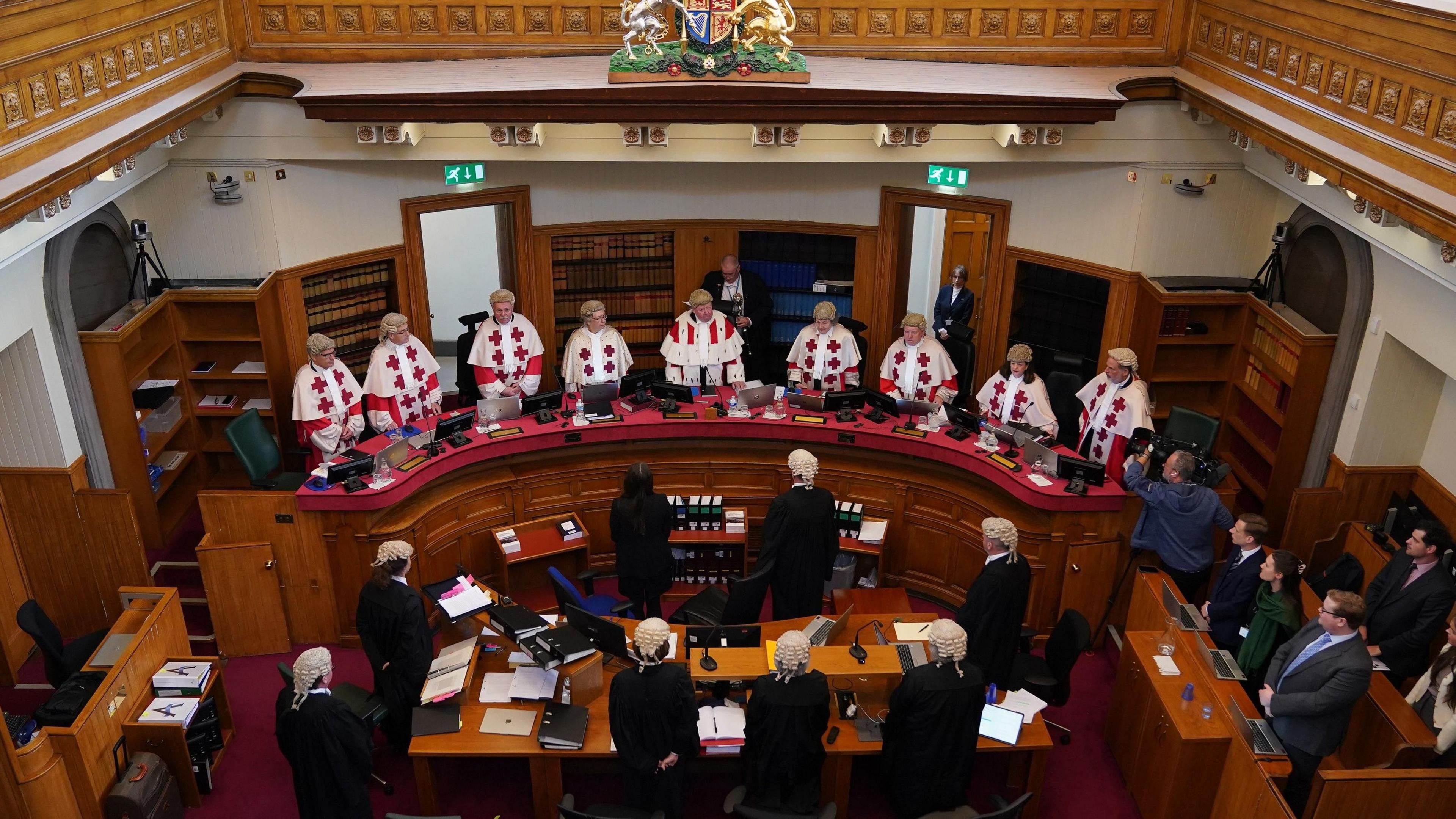 A court room with nine judges pictured behind a bench, with various officials facing them