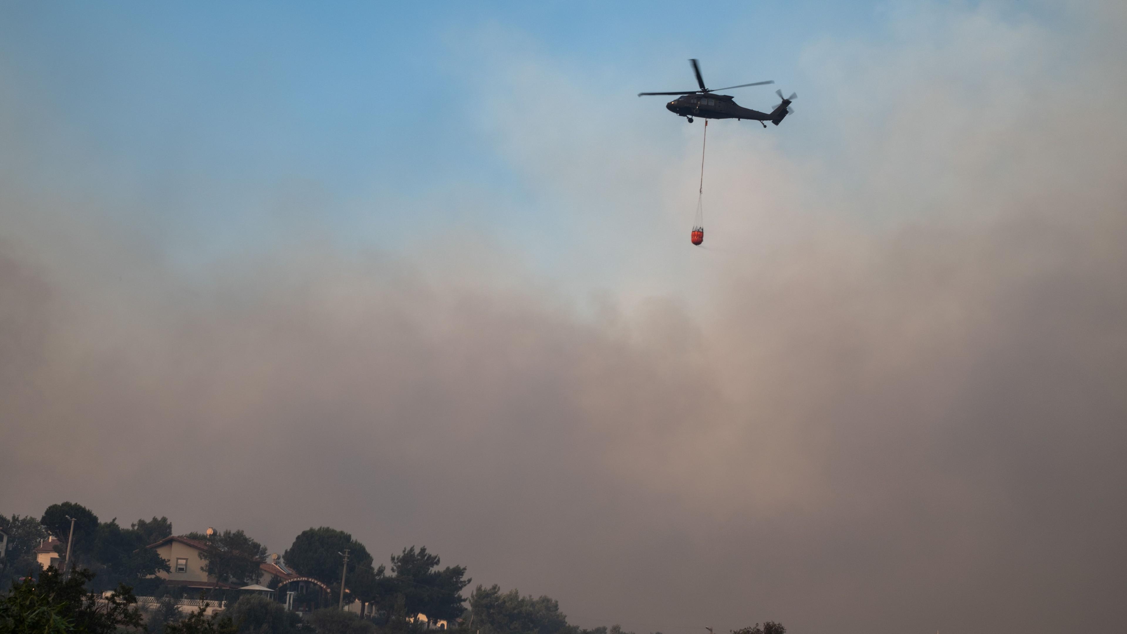 A helicopter carries water to put out the fire during the wildfires in the Seferihisar district of Izmir, Turkey, 30 June 2025. Turkish Forestry Minister Ibrahim Yumakli said the blaze in the Kuyucak and Doganbey areas of Izmir was fanned overnight by winds reaching 40-50 km/h (25-30 mph), leading to the evacuation of four villages and two neighbourhoods.