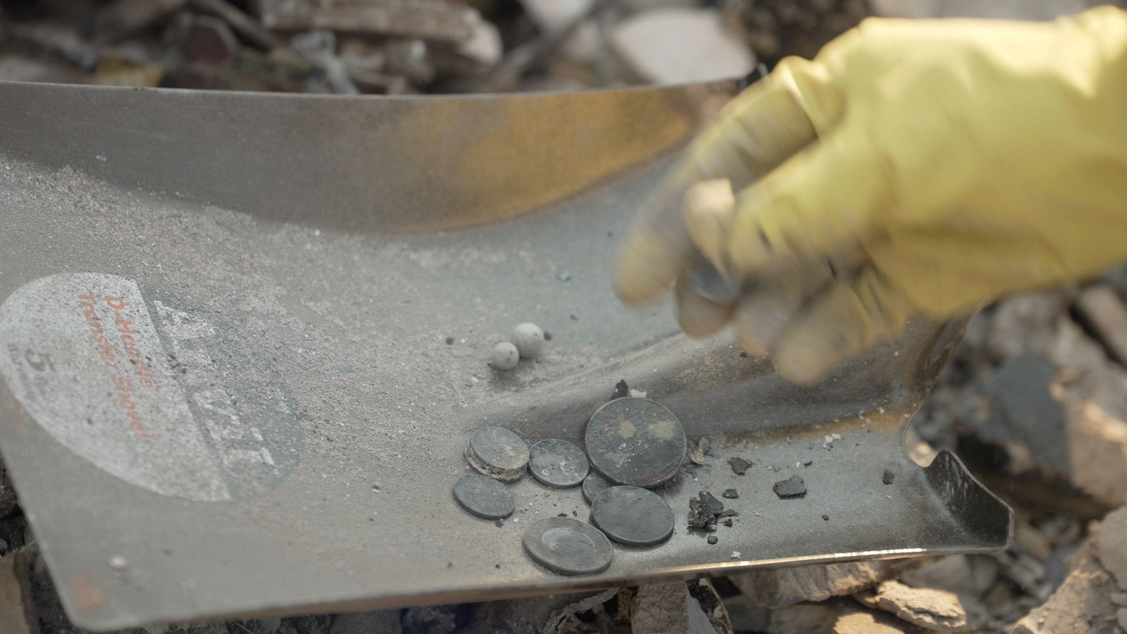 A marigold glove can be seen handling what appear to be coins which have been burnt 