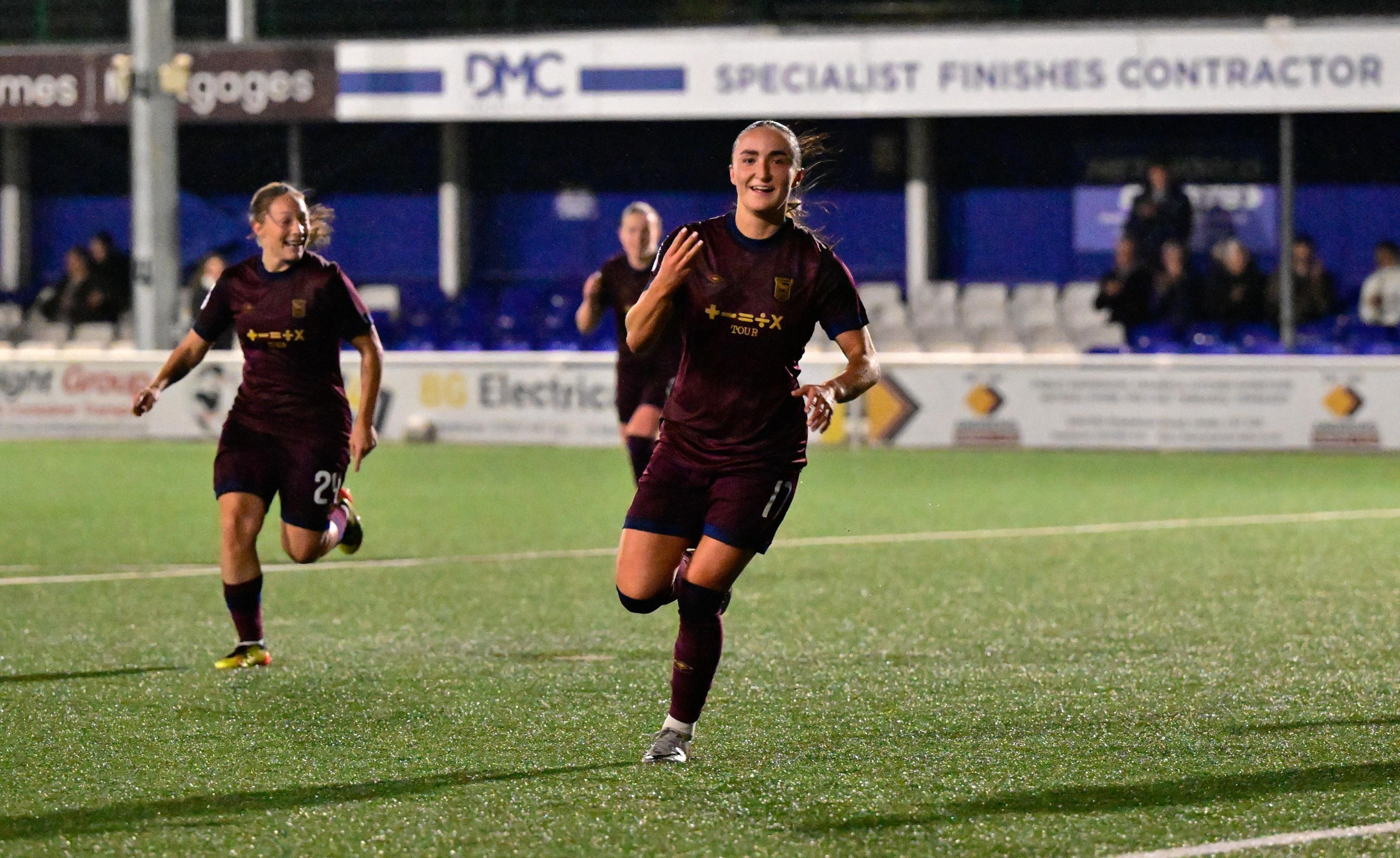 Sophie Peskett wearing a burgundy kit and celebrating while holding up three fingers 