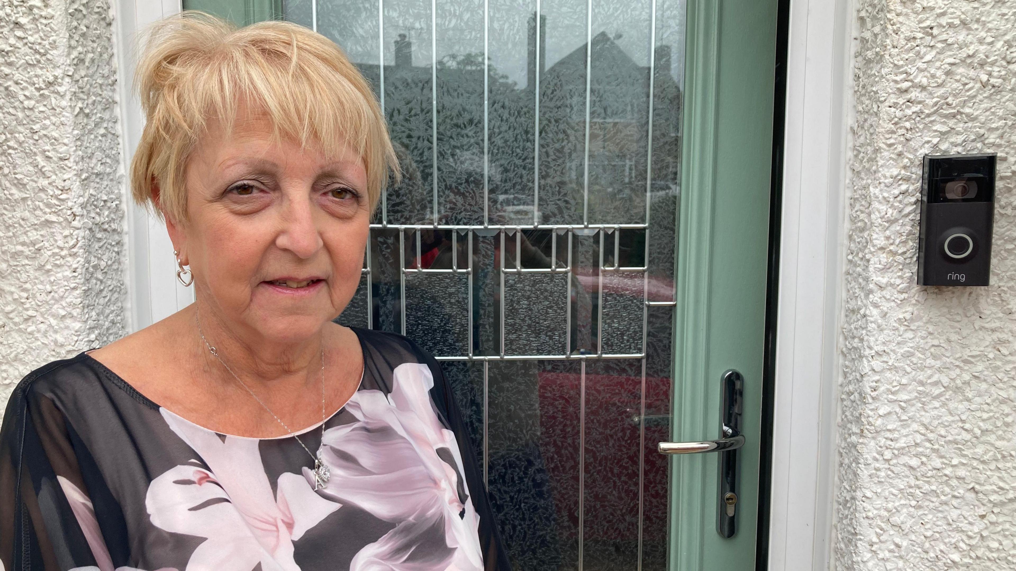 A woman with blonde hair stands outside her turquoise front door