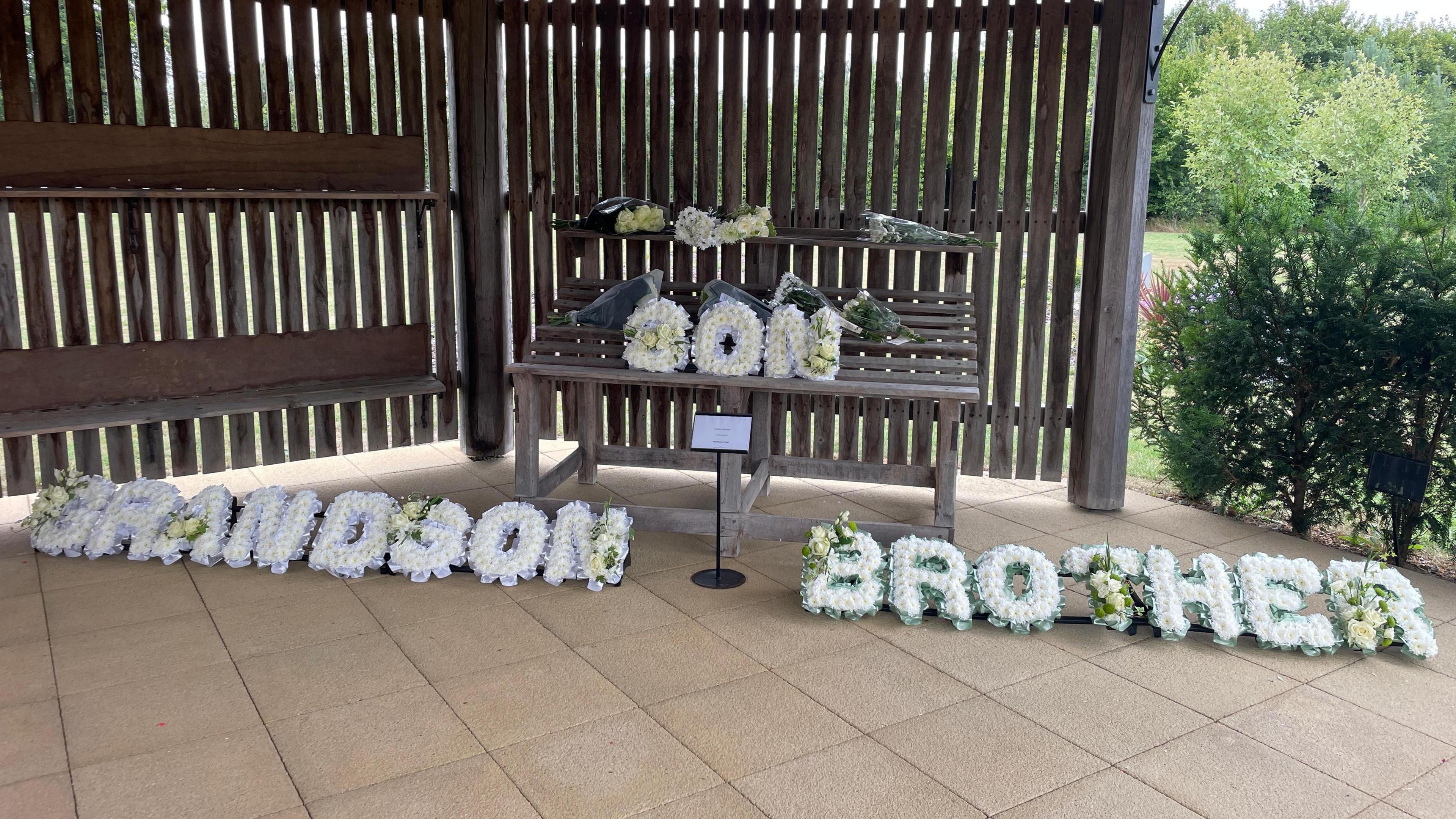 Three flower wraiths are in the image. Two of them are on the floor with the one on the left saying grandson and the one on the right saying brother. There is another in the middle on a wooden bench which says son.