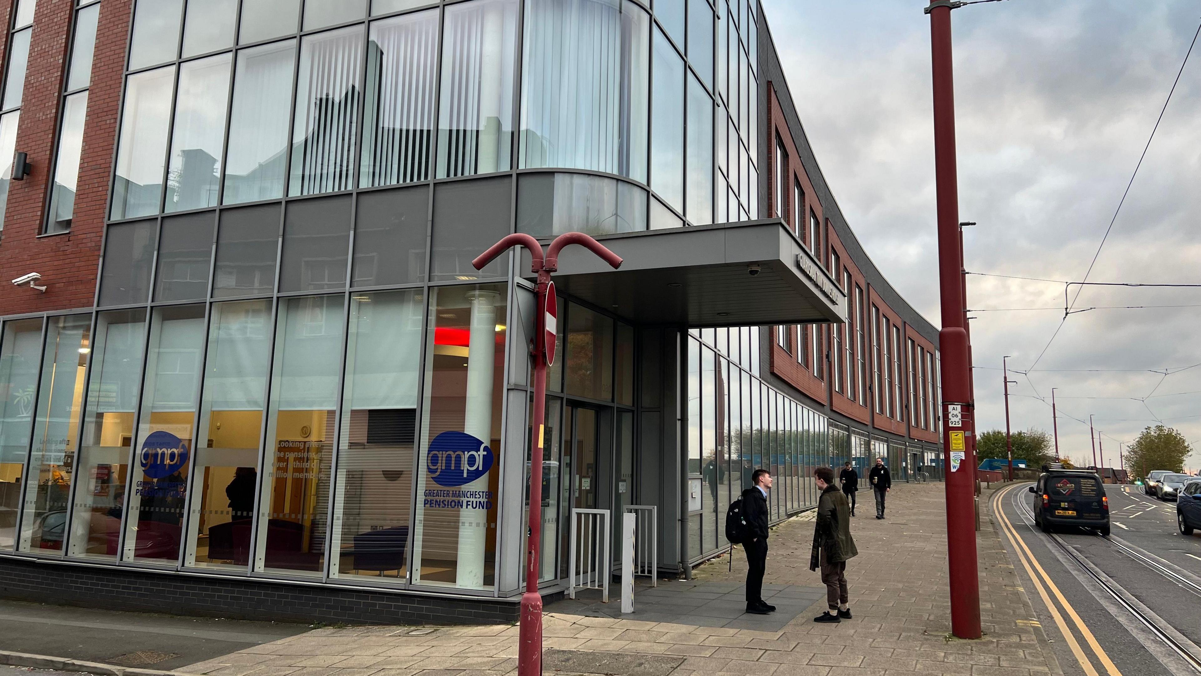 A street view of two people stood on a pavement talking outside of Tameside Council's offices on an overcast day