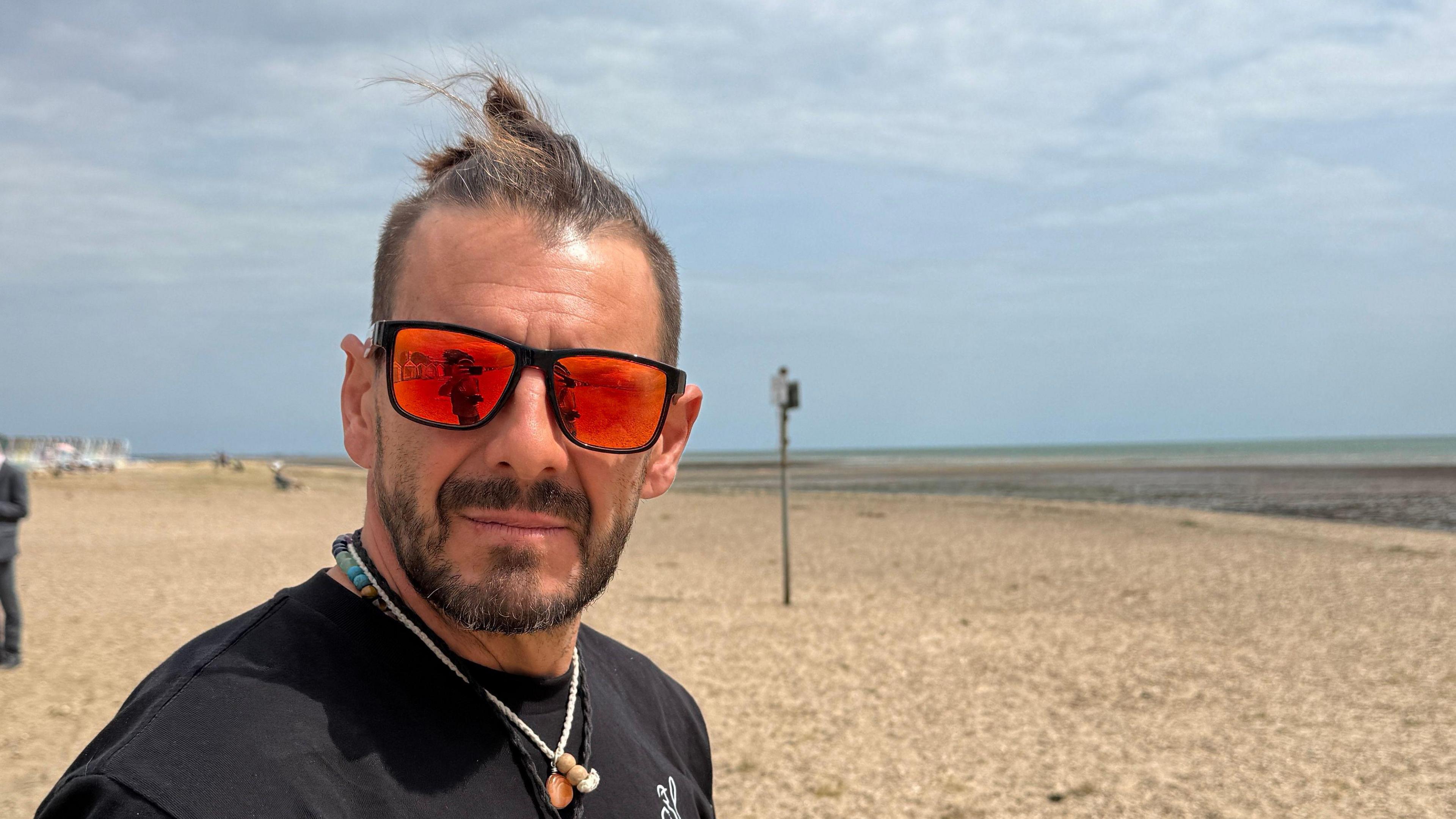 A man wearing sunglasses and a black shirt while standing on the beach.