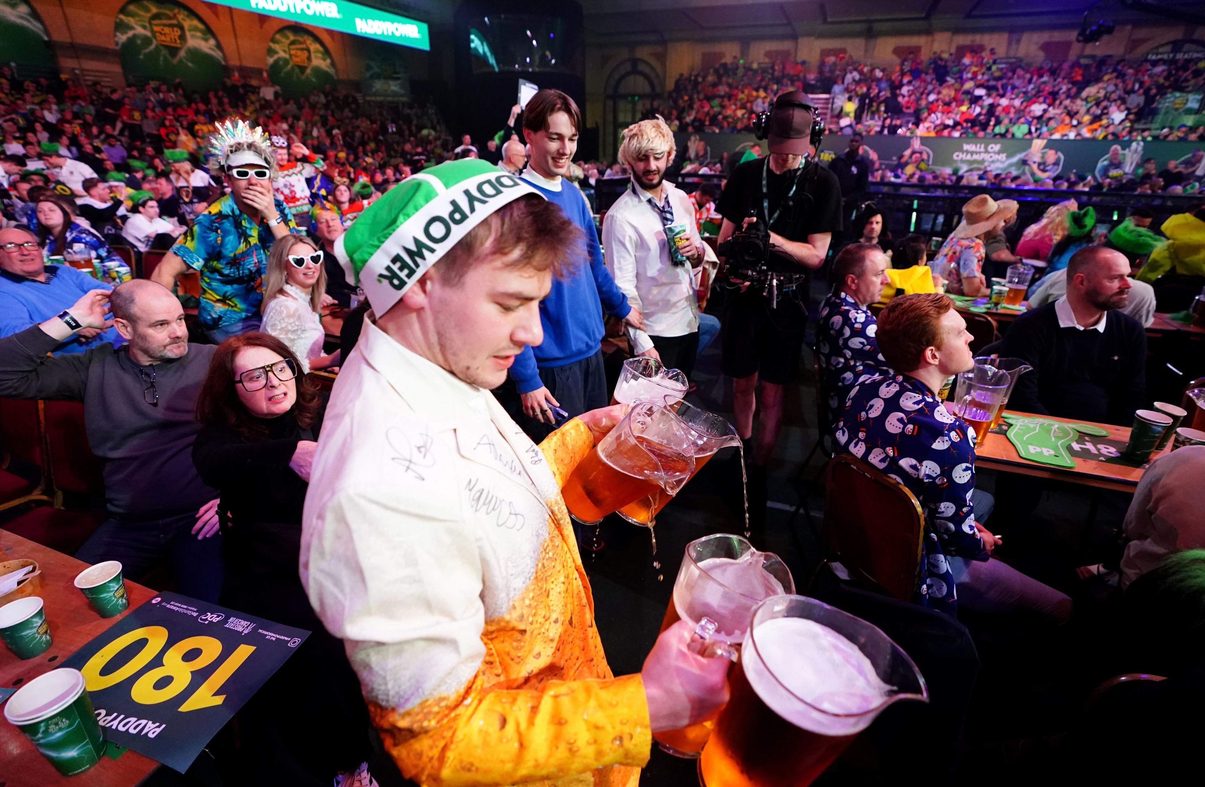 A man dressed in a beer glass costume holds four jugs of beer