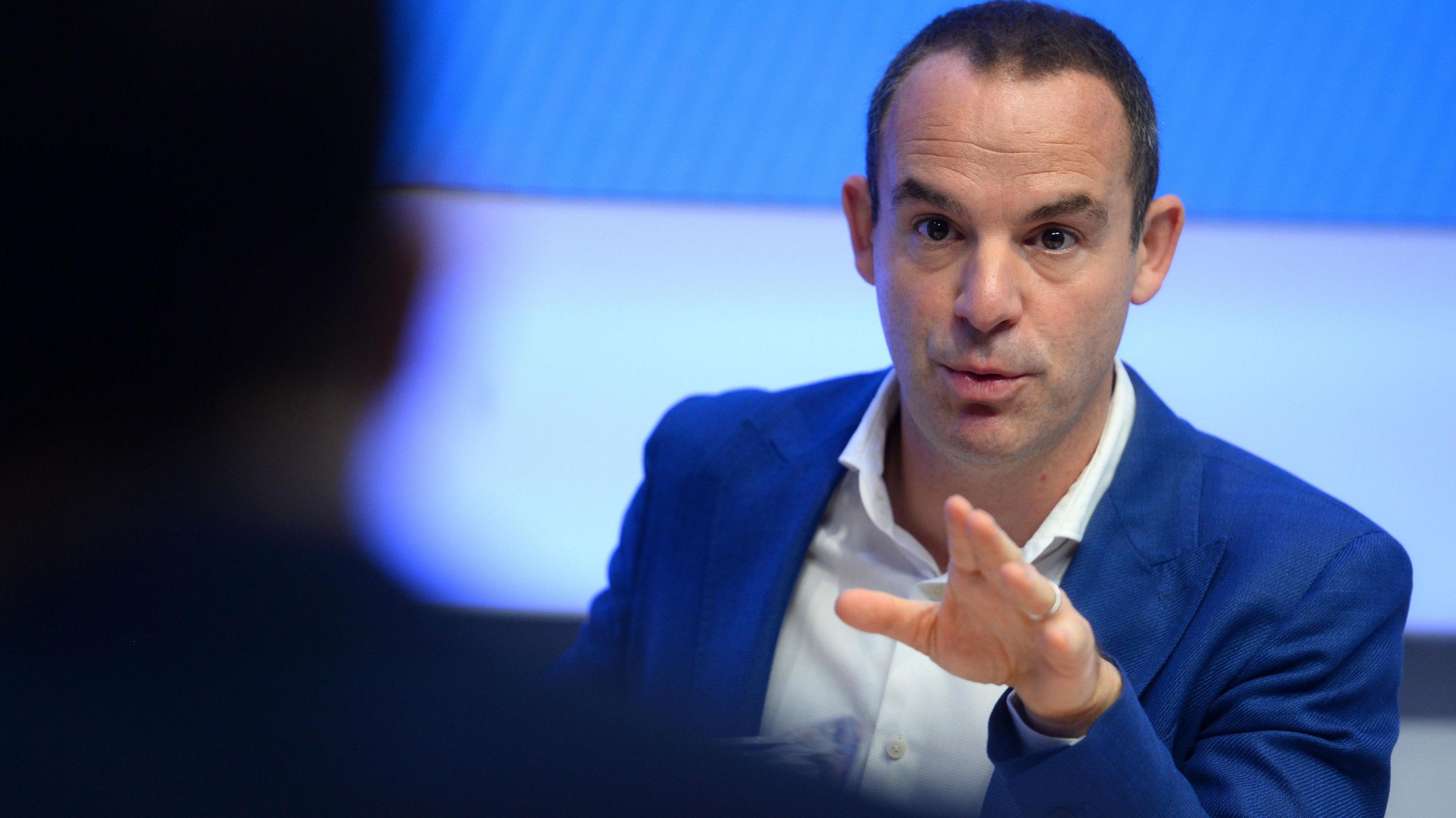 Personal finance journalist and campaigner Martin Lewis wears a blue suit and a white shirt while speaking at a press conference.