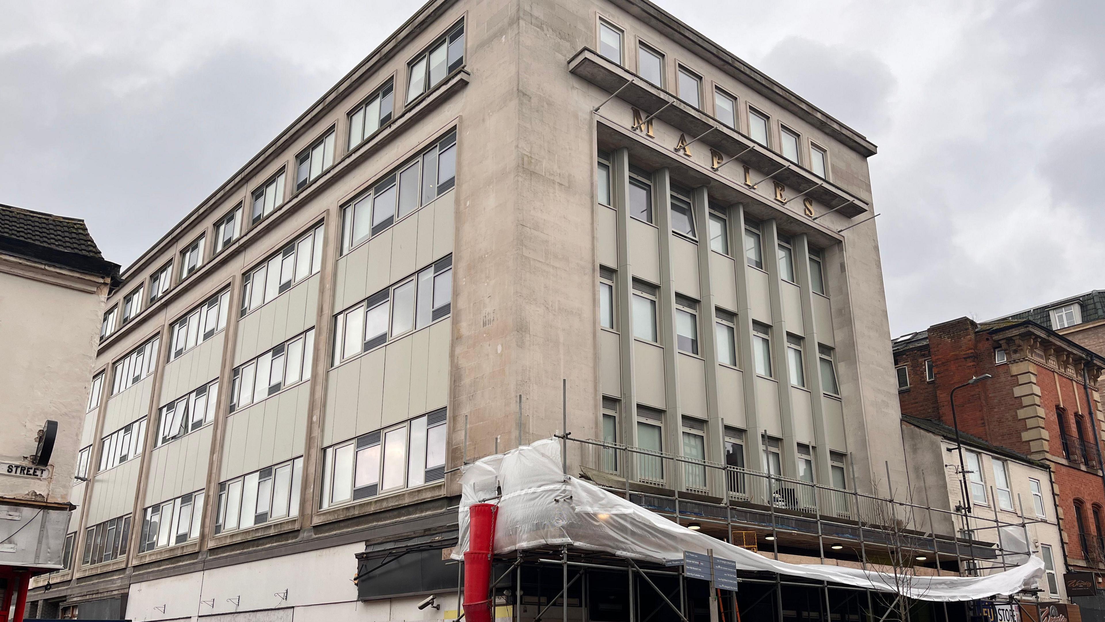 A large white stone five-storey building with scaffolding at ground level 