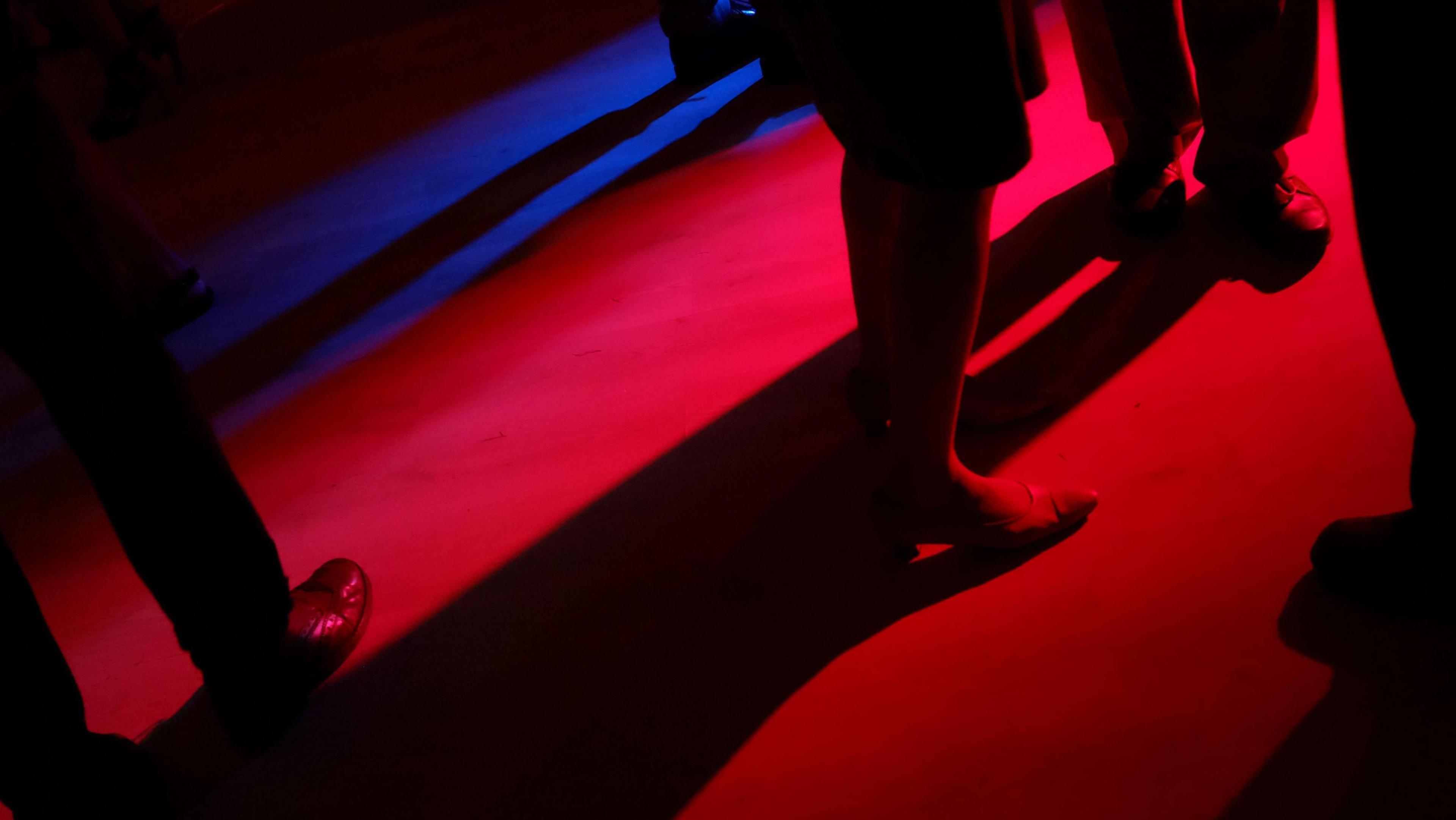 People's legs on a darkly-lit dance floor.