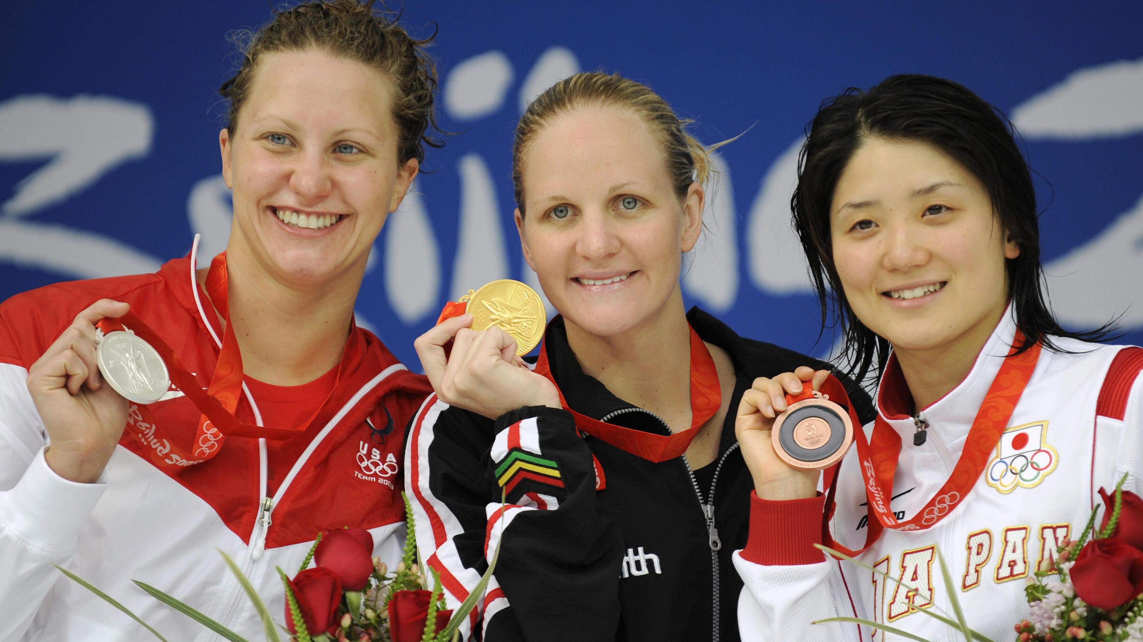 Swimmers Margaret Hoelzer, Kirsty Coventry and Reiko Nakamura hold up their silver, gold and bronze medals respectively while standing on a podium at the Beijing 2008 