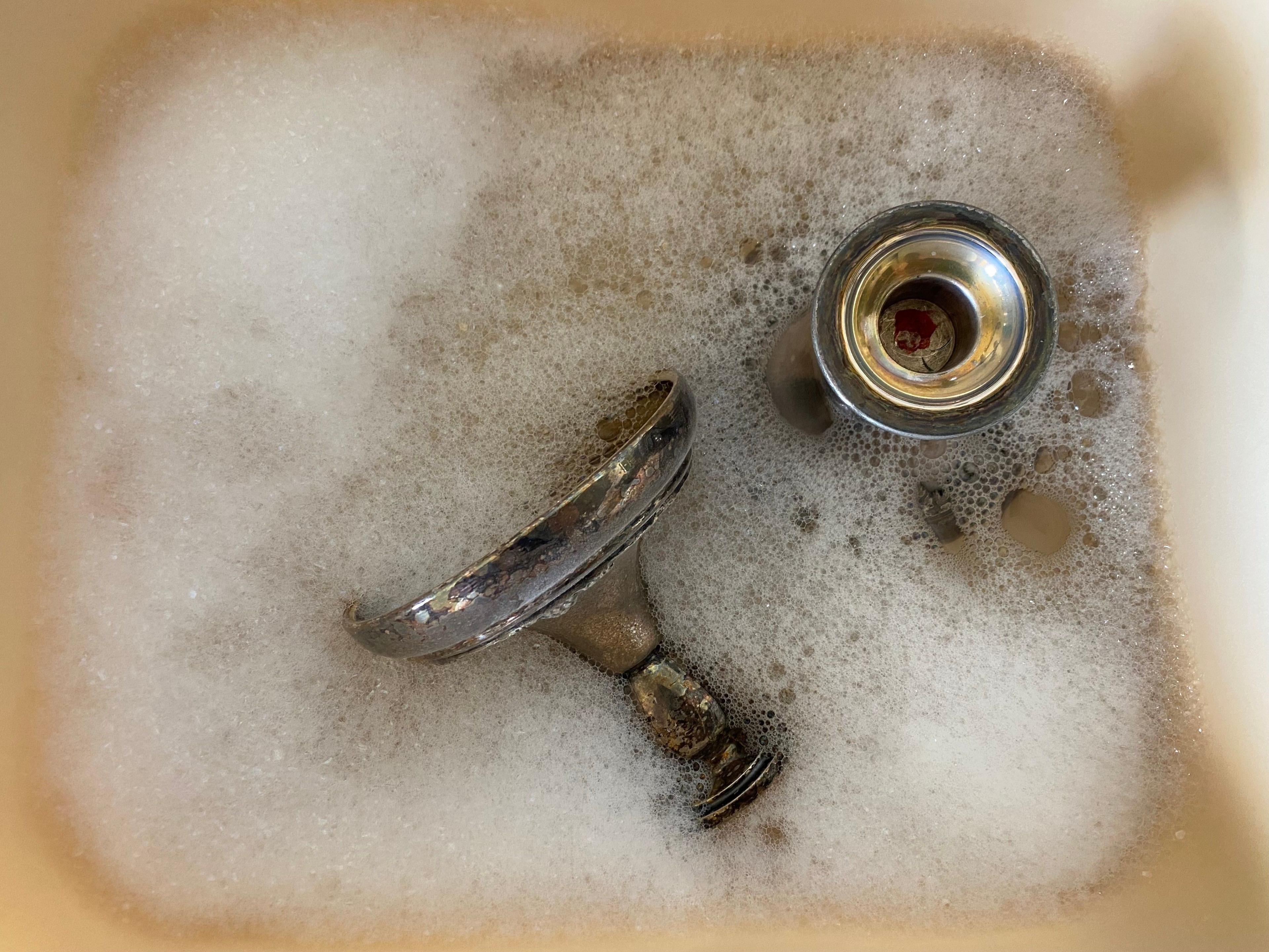 Silver candlesticks in soapy water in a sink