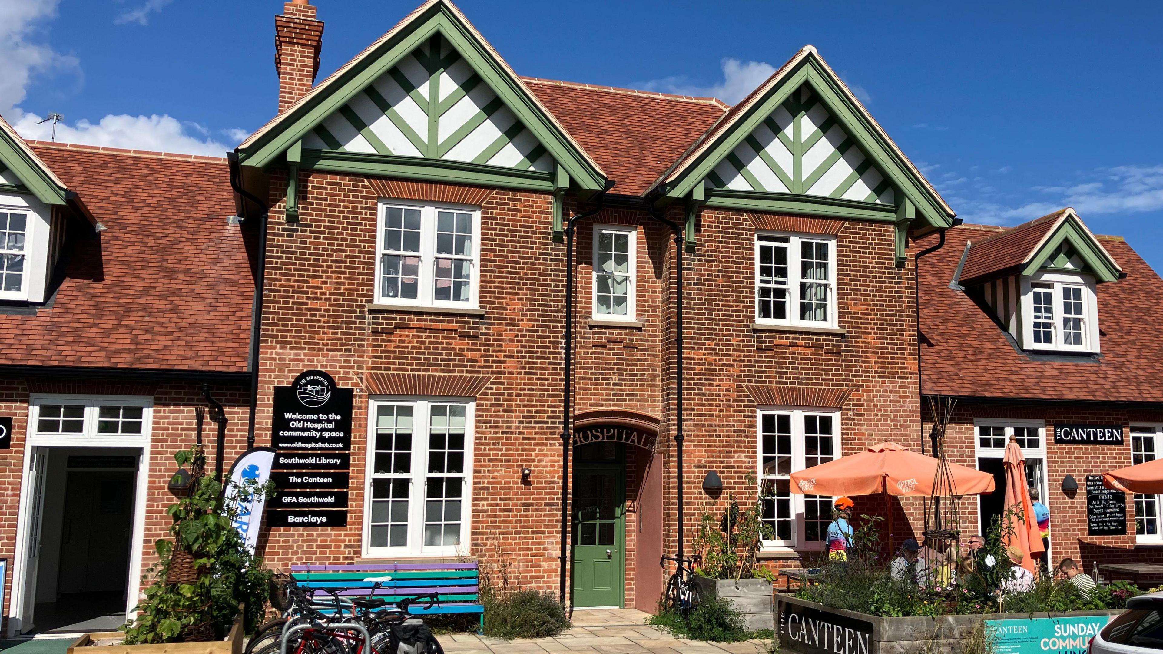 A brick, Victorian building, with green wooded boards on the roof and umbrellas outside.