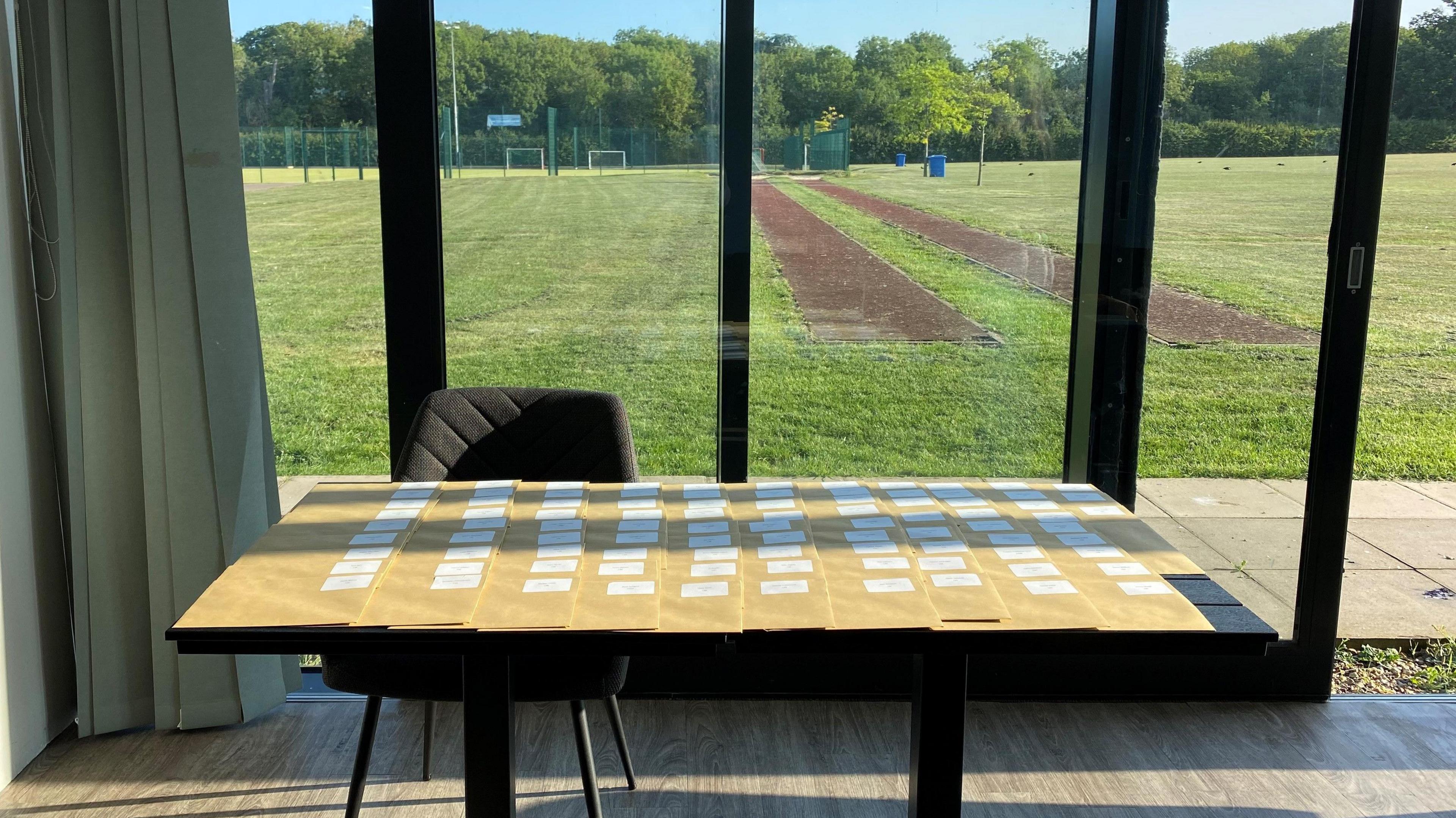 A table with brown envelopes placed on it- overlooking the sports field 