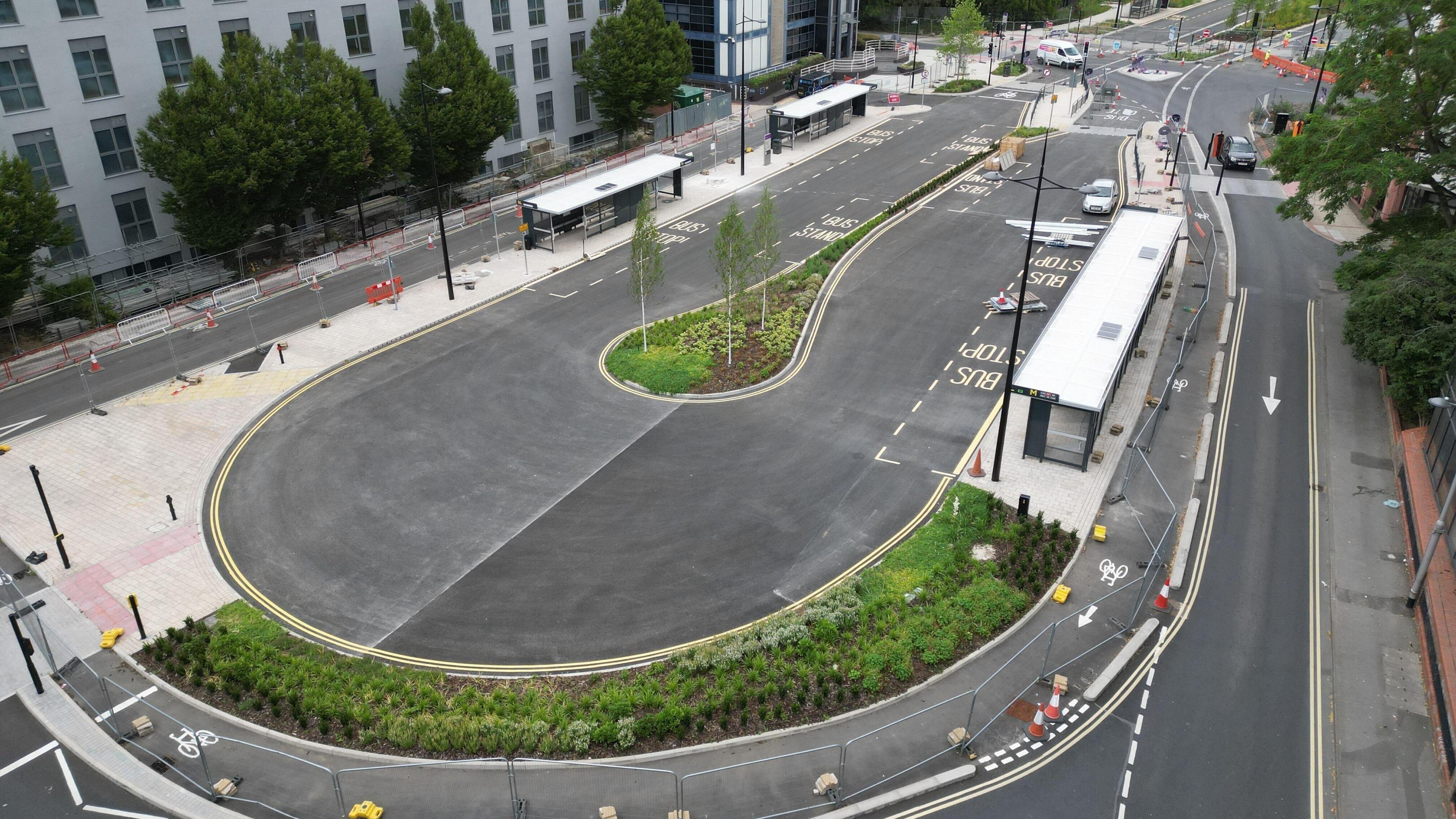 A new oval-shaped bus station in Swindon seen from a drone shot with newly-planted shrubbery, red cones and new markings for bus stops. The area is fenced off.