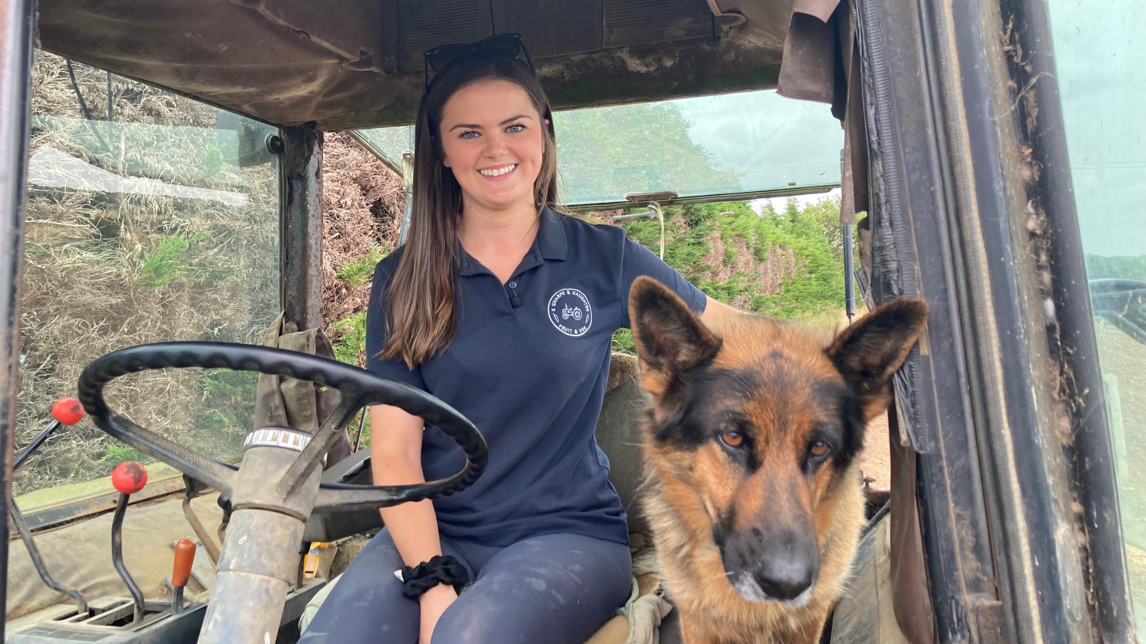Bethany Sharpe sitting in a tractor with her arm around her Alsatian dog, Willow