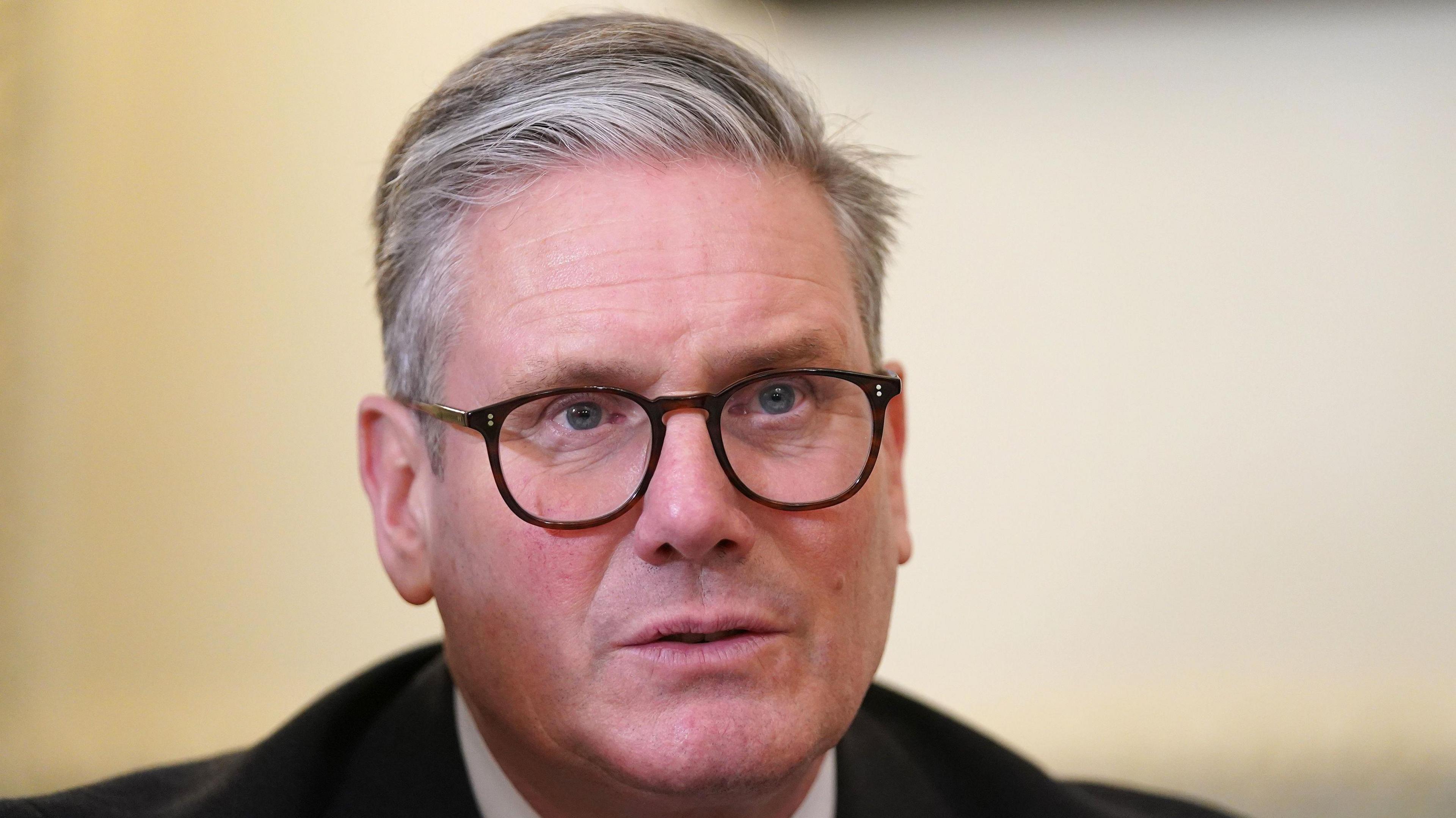 Sir Keir Starmer is pictured sitting in a room looking away from the camera. He is wearing black glasses and a black suit with a white shirt underneath