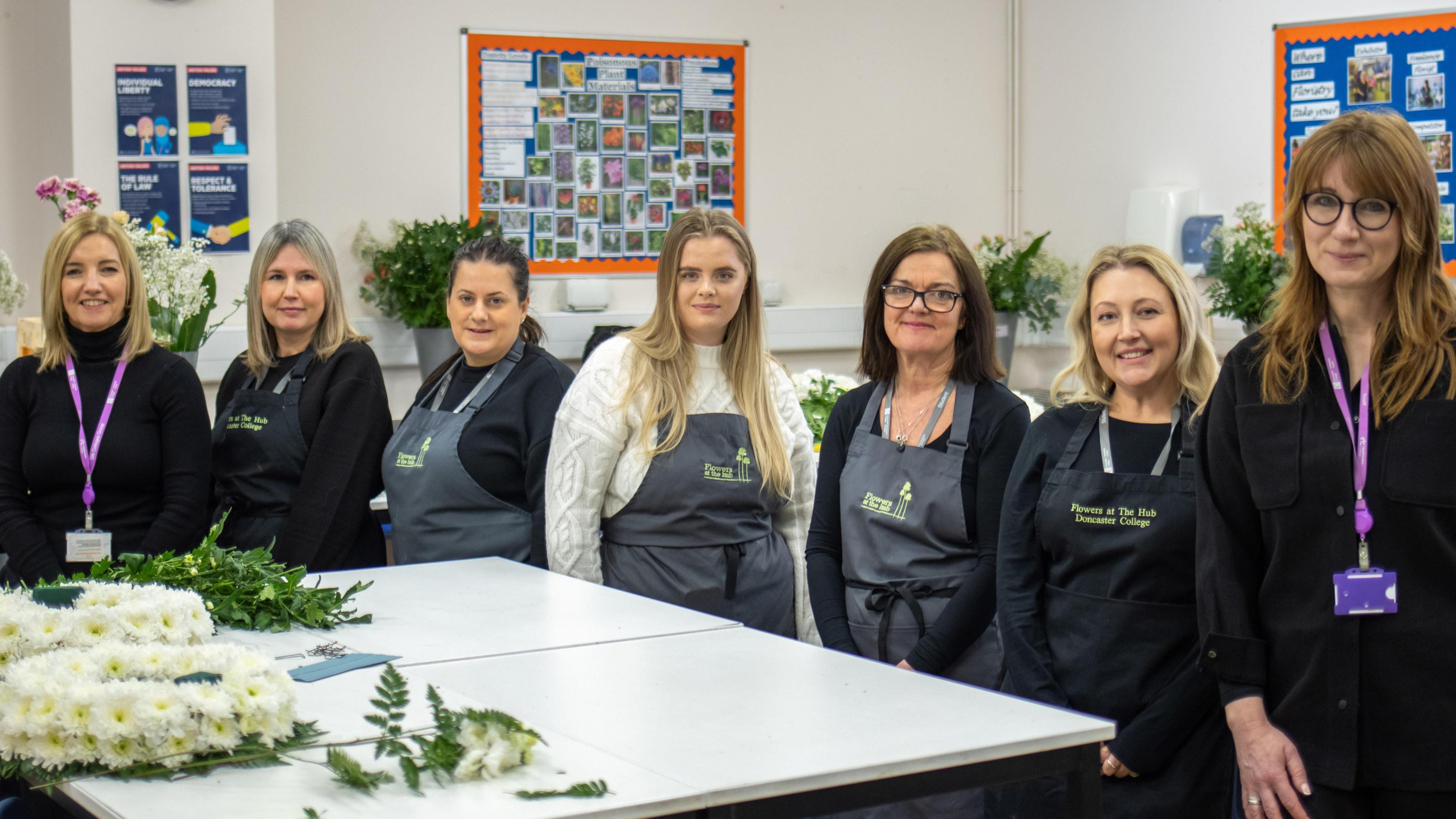 Seven women standing at a table with flowers on its top, they are Doncaster College's Floristry Team for the Cheslea Flower Show