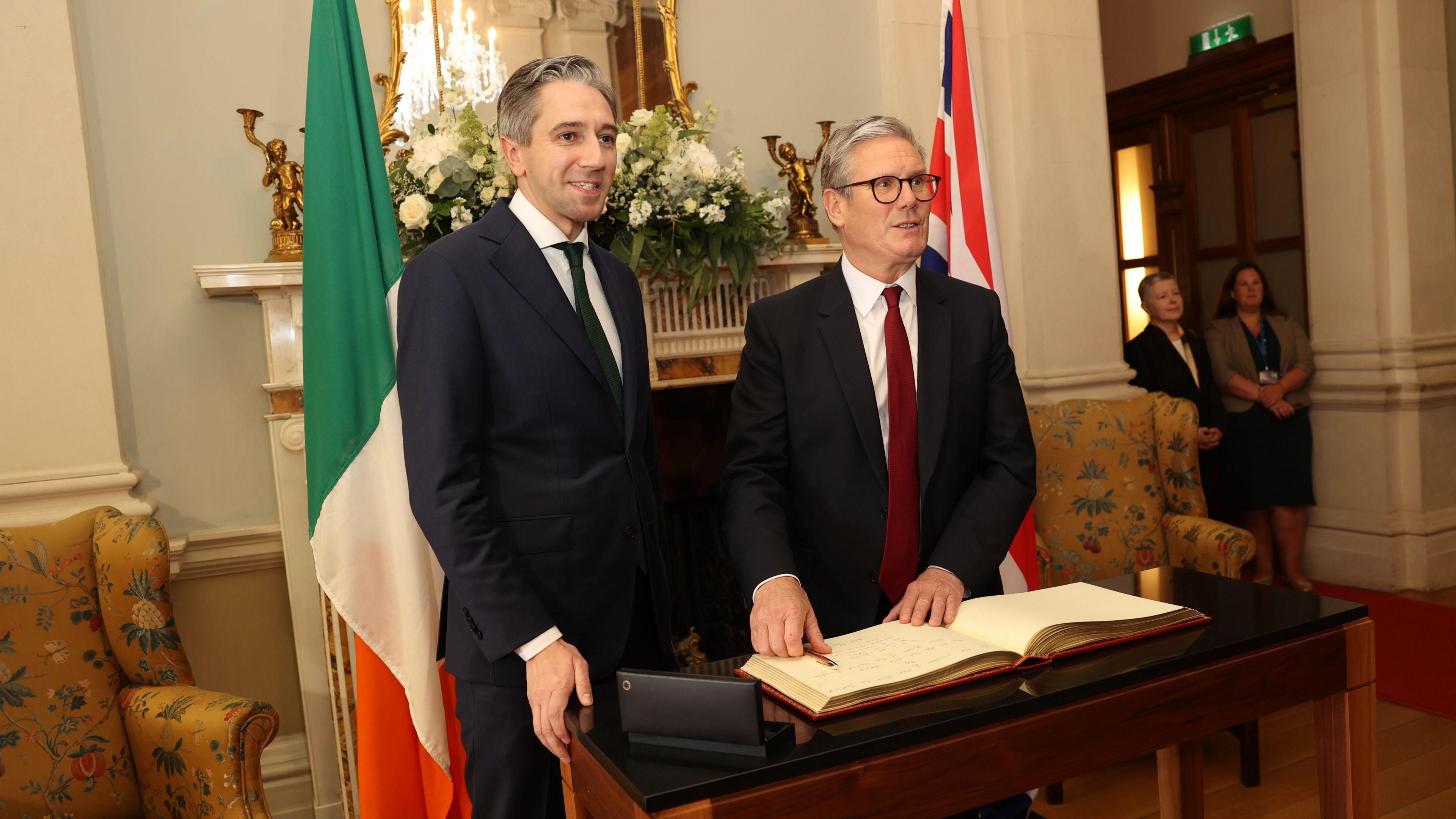 Simon Harris stands beside Sir Keir Starmer as the UK prime minister signs the visitors' book in Farmleigh House, Dublin