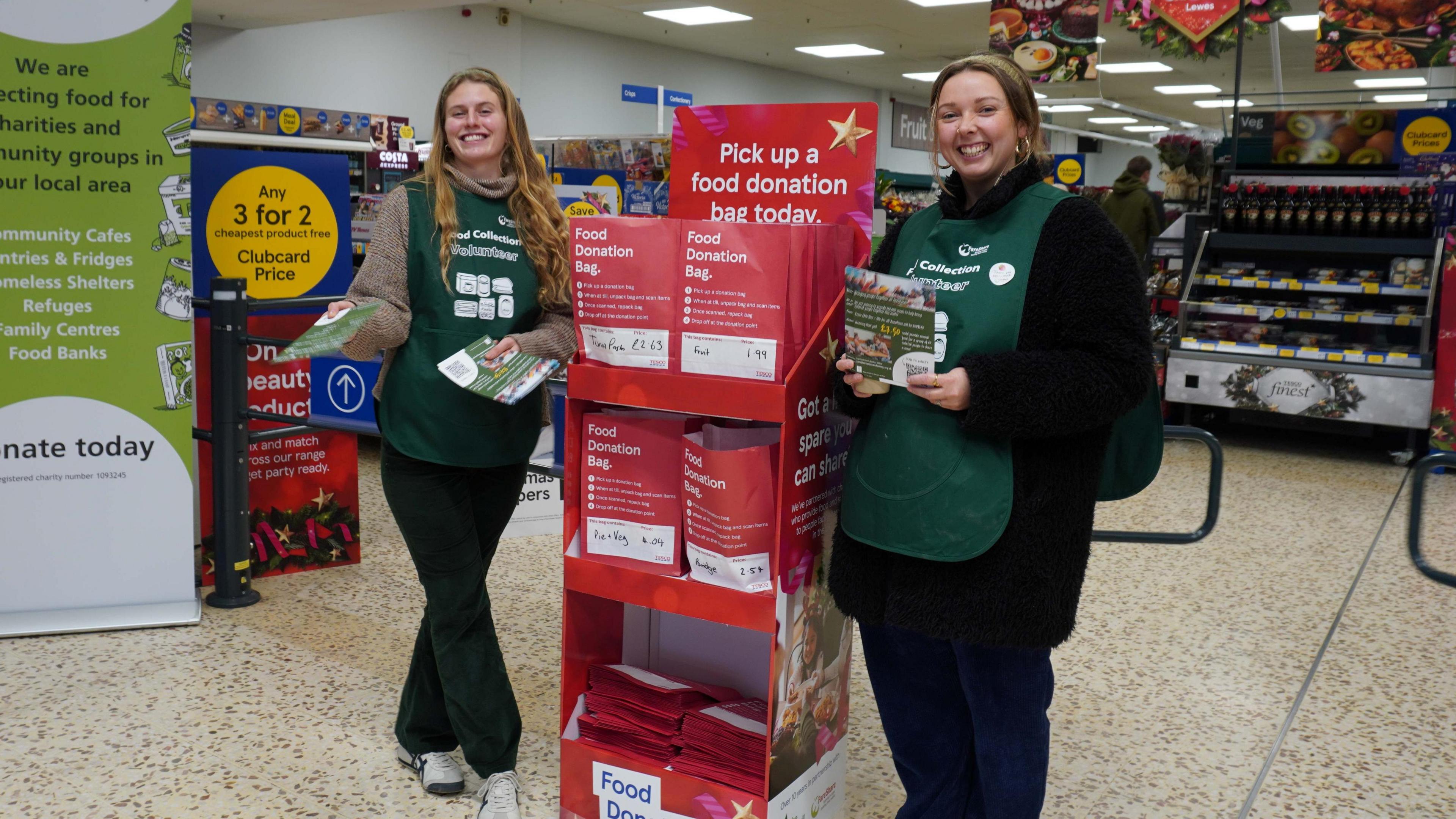 Two female volunteers in green lanyards standing in a supermarket 