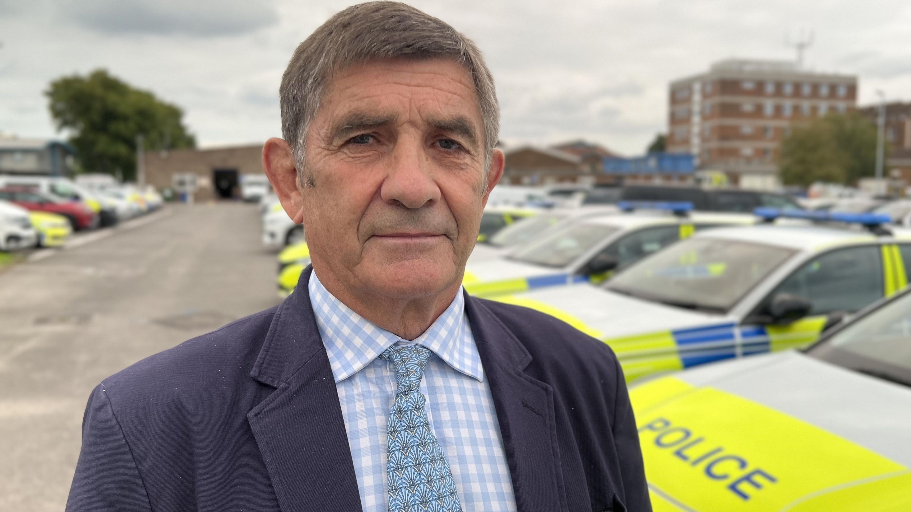 Police and Crime Commissioner, Philip Wilkinson, standing amongst parked police cars wearing a navy blue suit