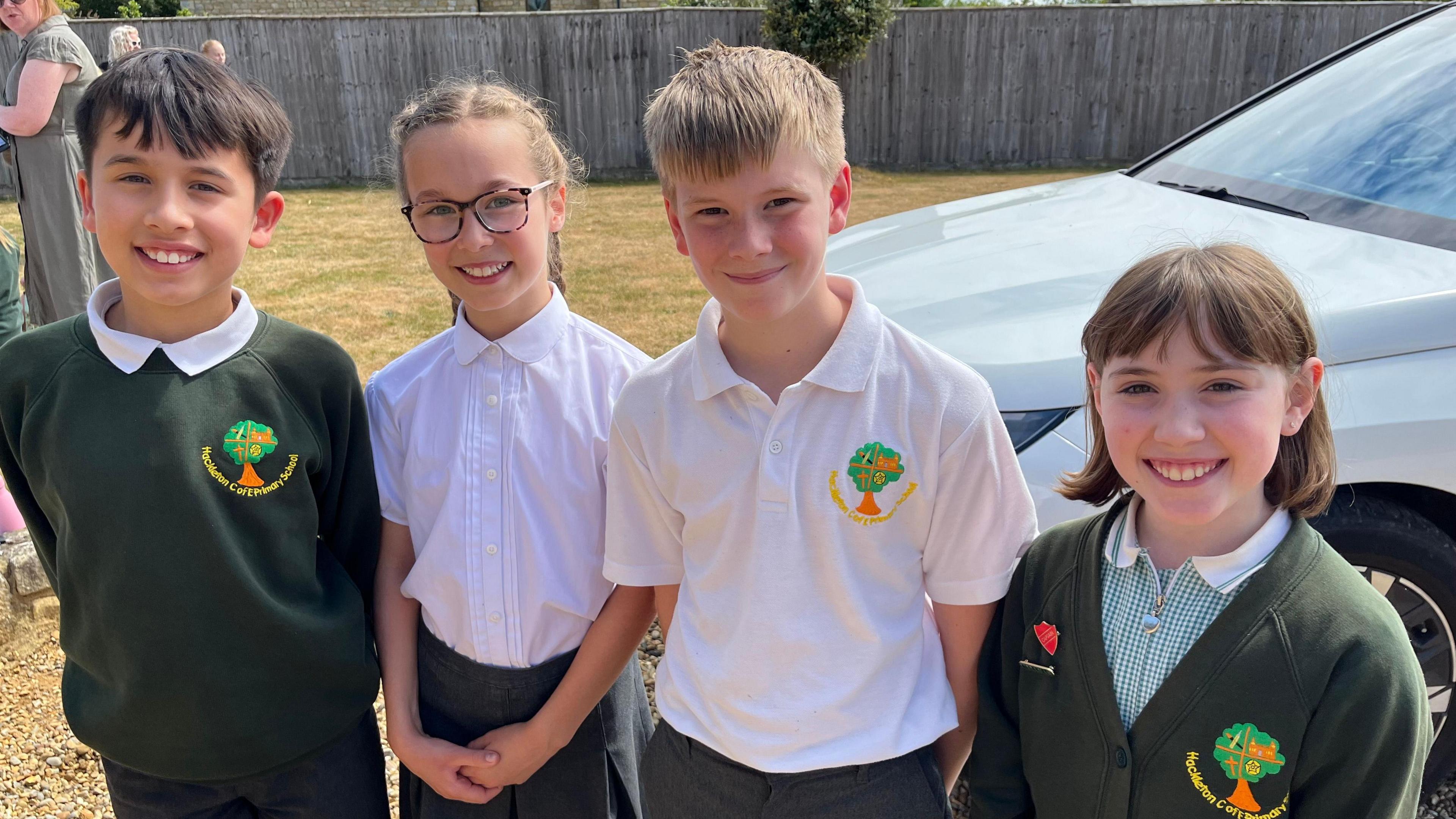 Four children in green jumpers and white polo shirts smile at the camera.
