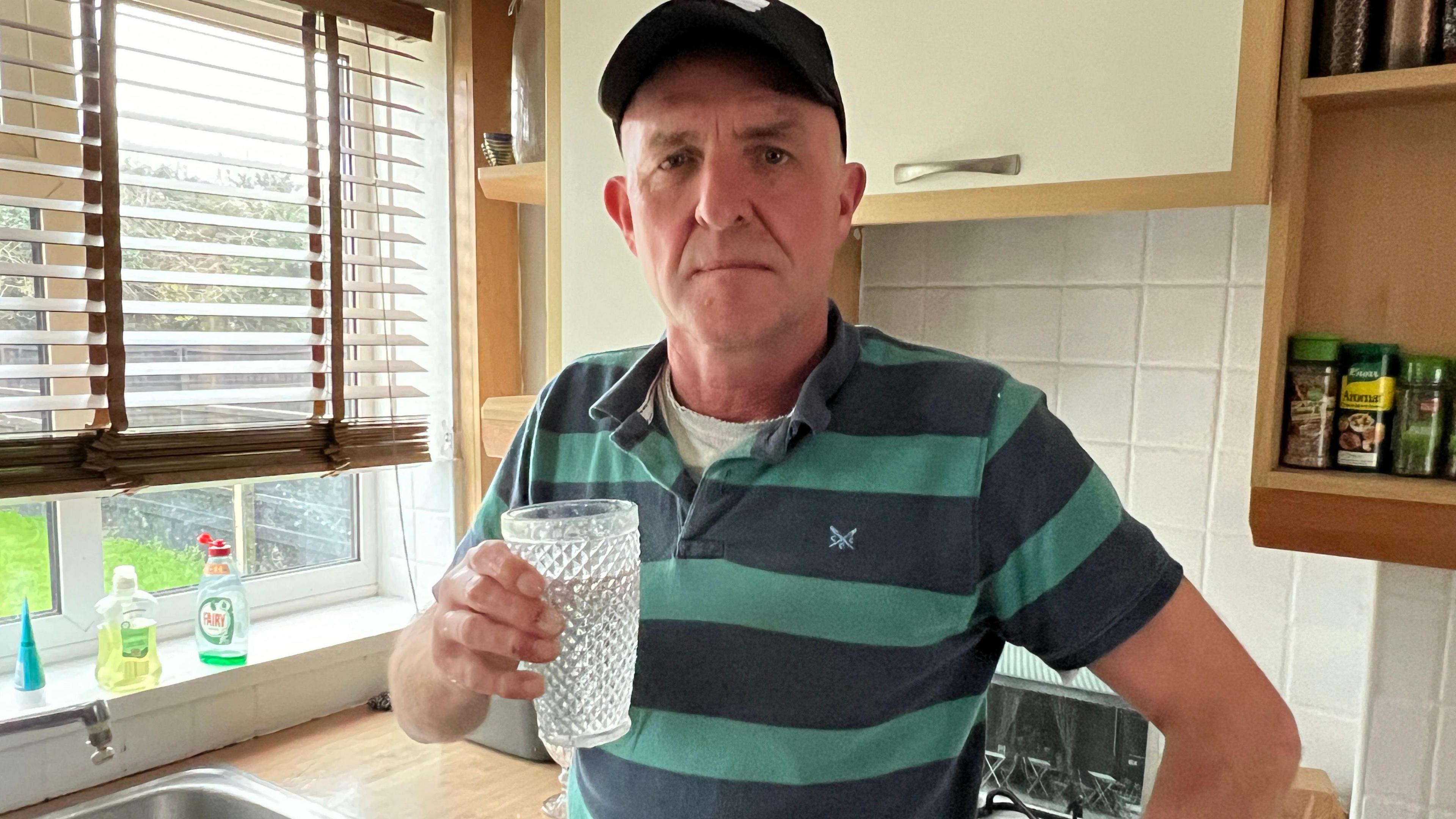 A man holding a large glass of water as he stands in his kitchen in Bourton-on-the-Water in the Cotswolds