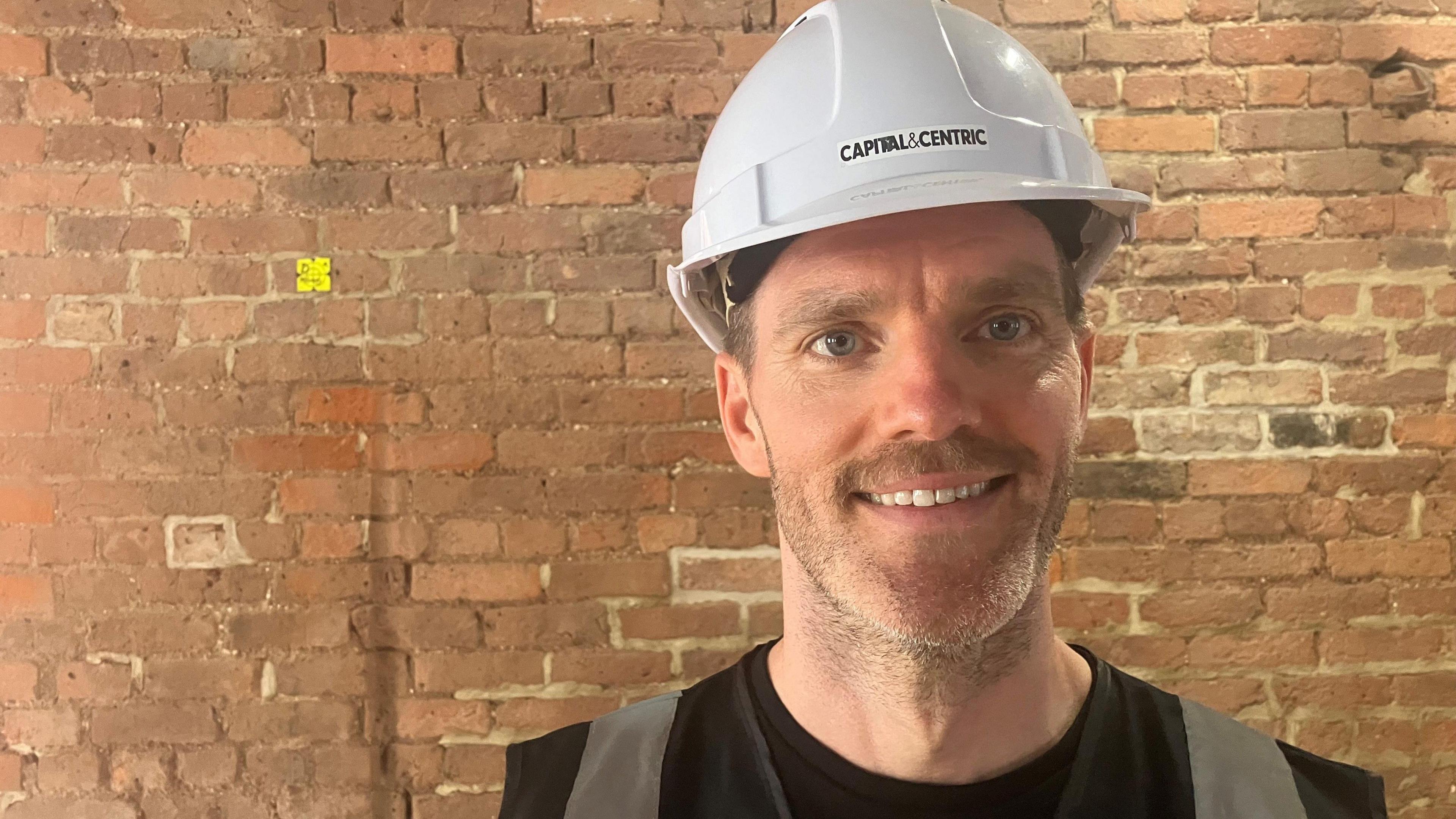 Photograph of Tim Heatley from Capital and Centric. He is pictured in a hard hat in front of a brick wall at Talbot Mill in Castlefield.