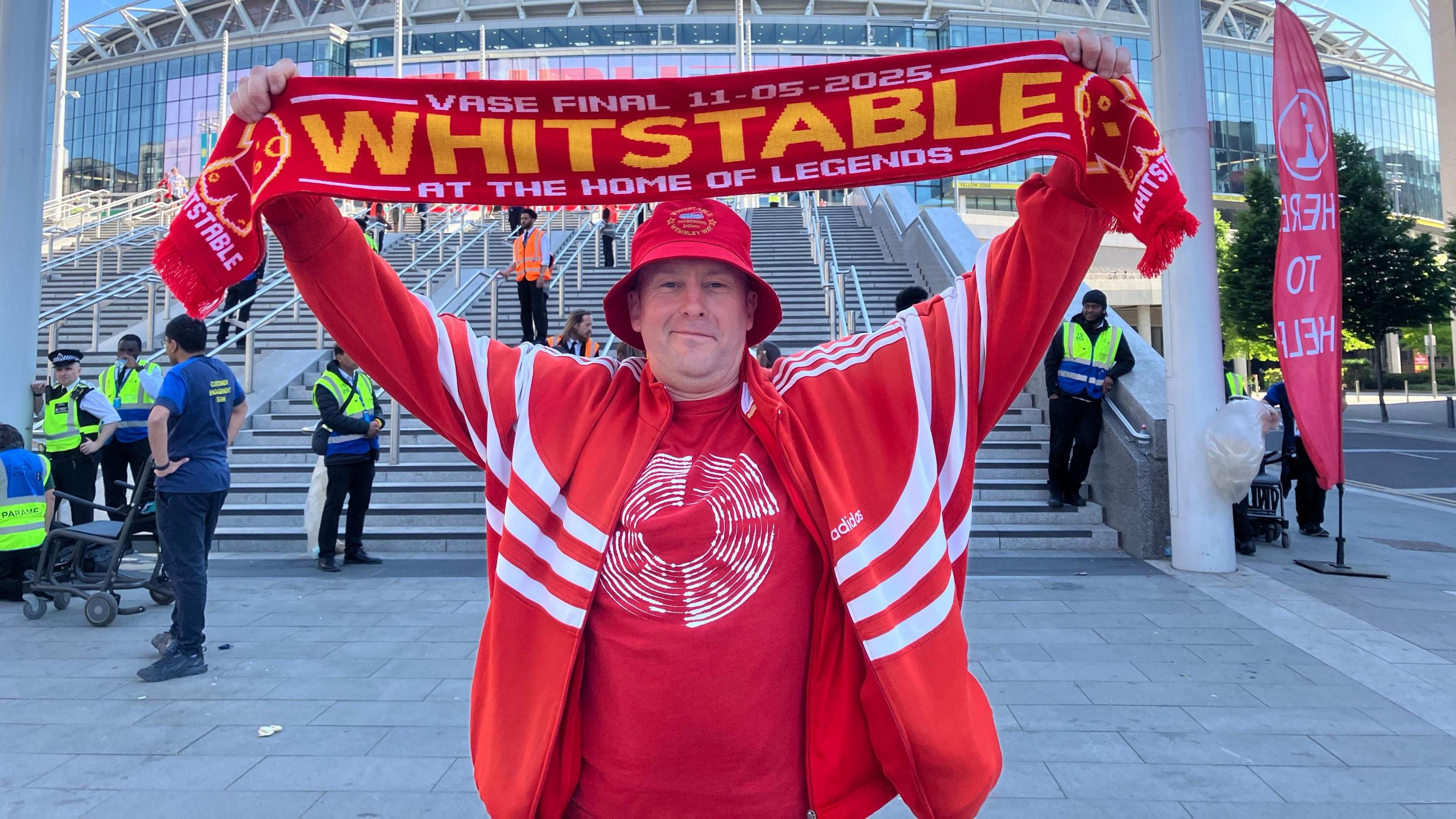 A man in red holding a red scarf which reads "Whitstable".