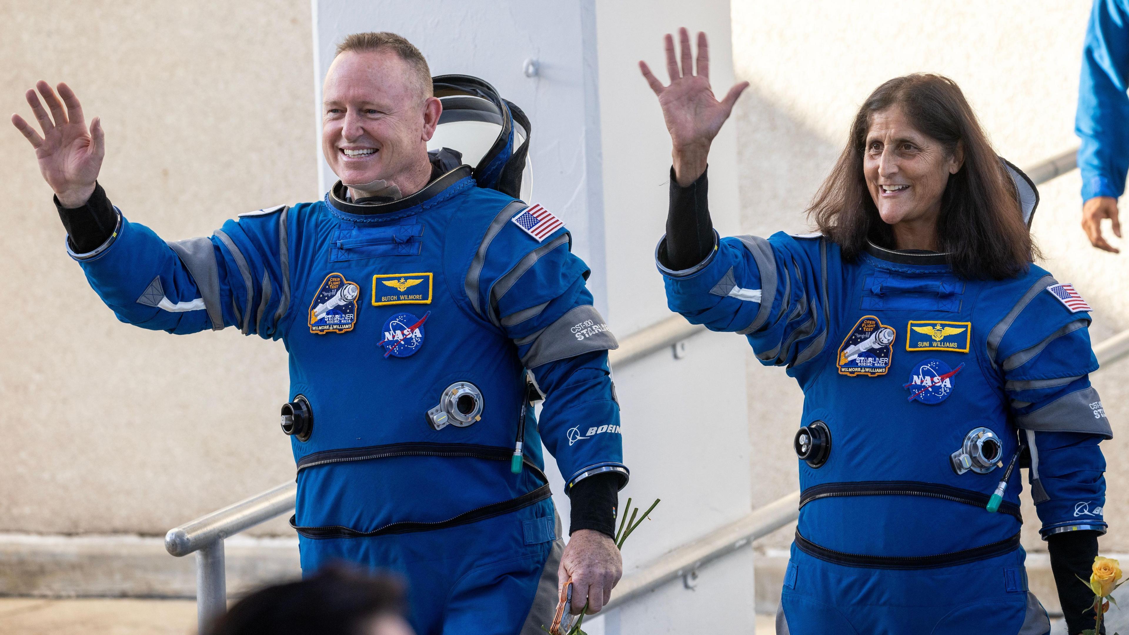 suni and butch waving in their space suits