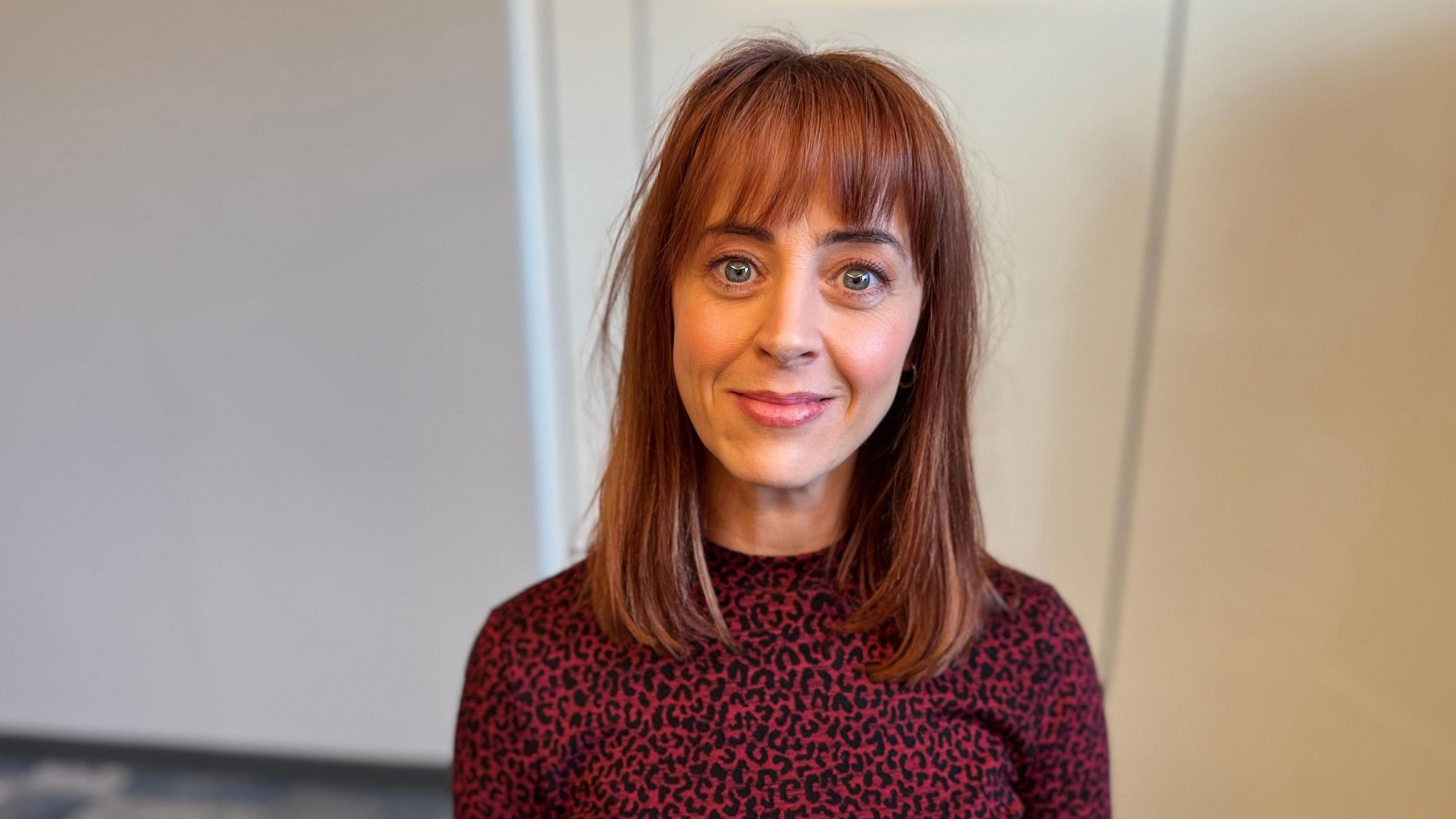 Mae Siwan Morris yn sefyll yn erbyn wal gwyn. Mae hi'n gwisgo ffrog coch a du gyda phatrwm croen llewpard. Mae ganddi wallt brown golau. Mae hi'n gwenu.