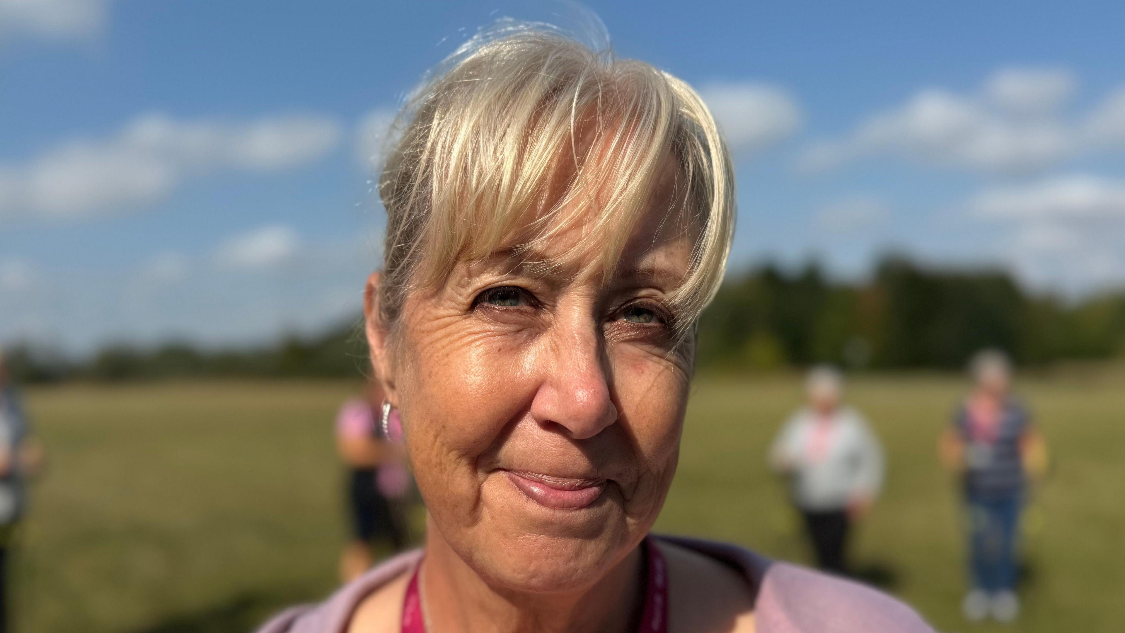 A smiling Karen Brimson looks straight into the camera while standing in a field.