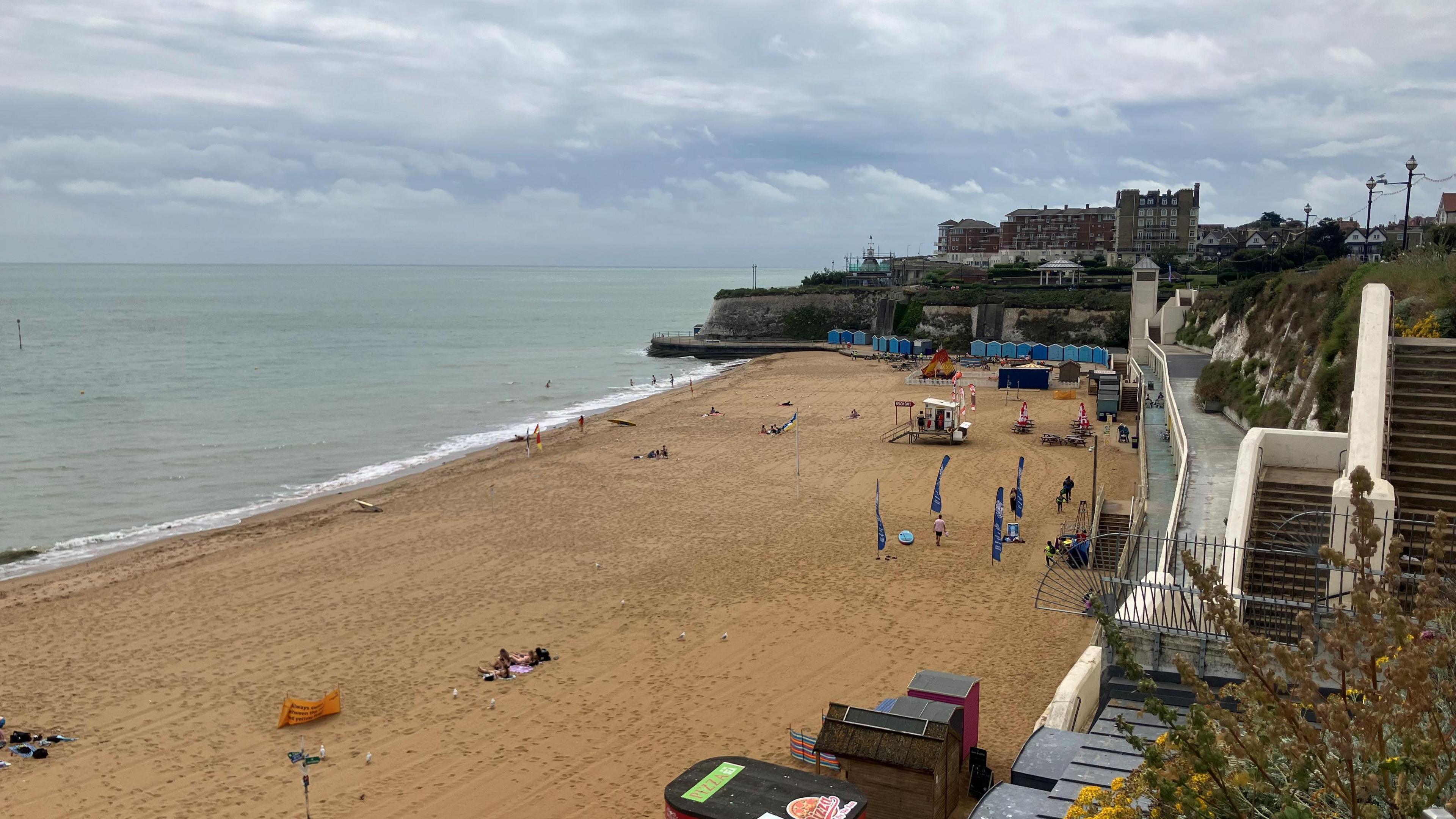 A beach with stairs to the right of it. The sky is blue and cloudy.