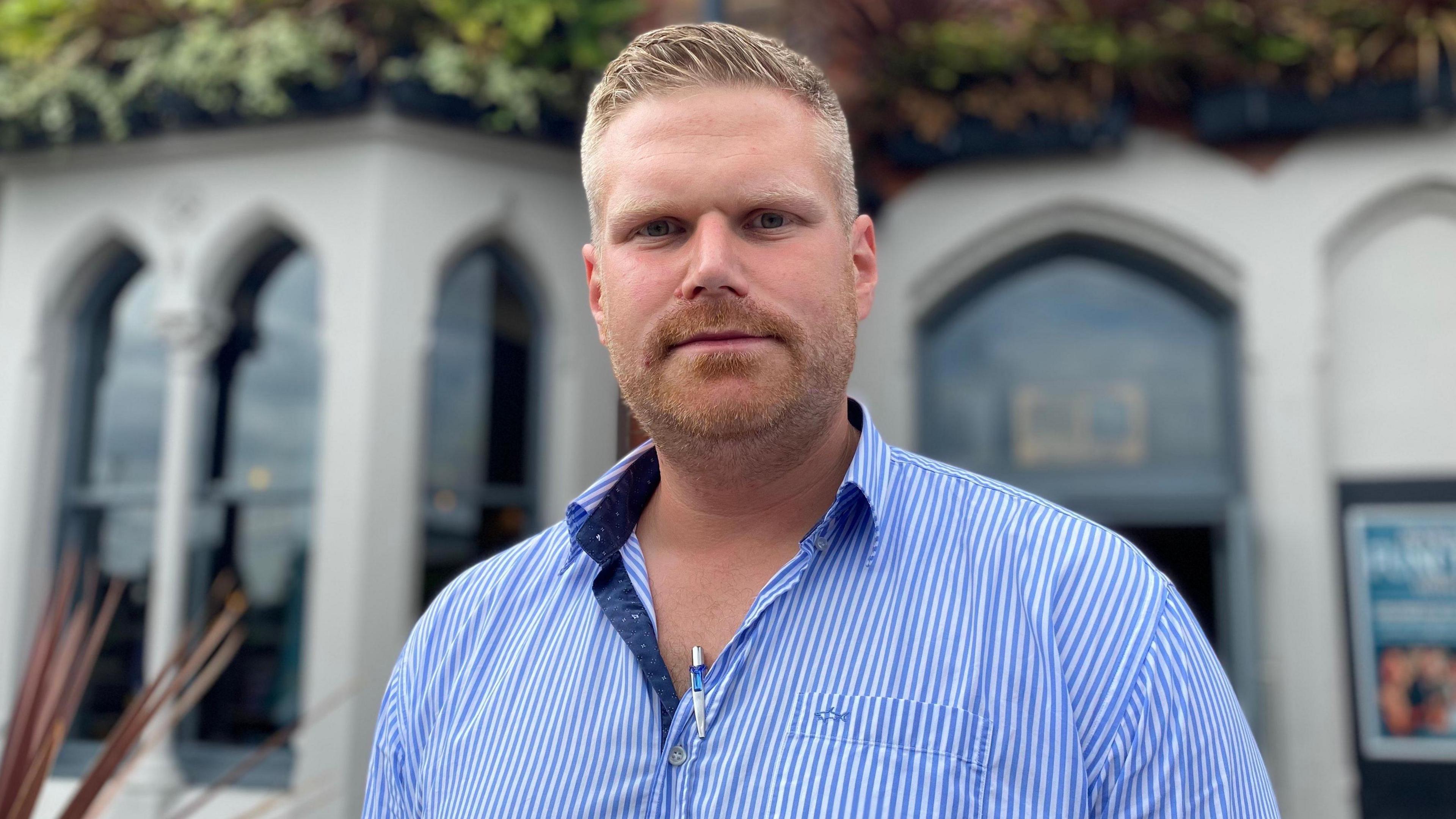 A man in a blue and white striped shirt looks at the camera